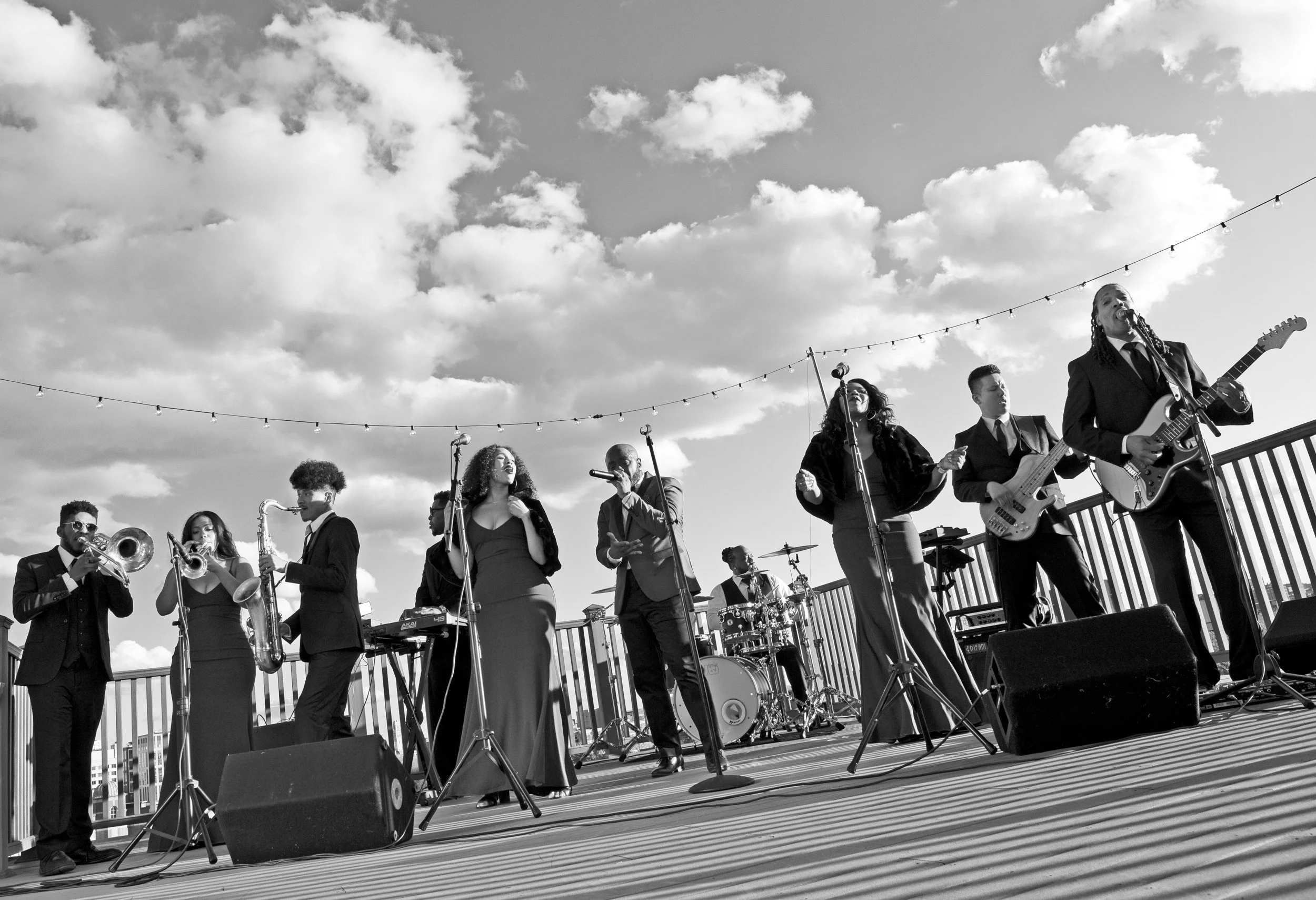 Black and white wide-angle of Soul of Boston band outside on rooftop in Boston with sky and clouds as background - Hank Agency Group