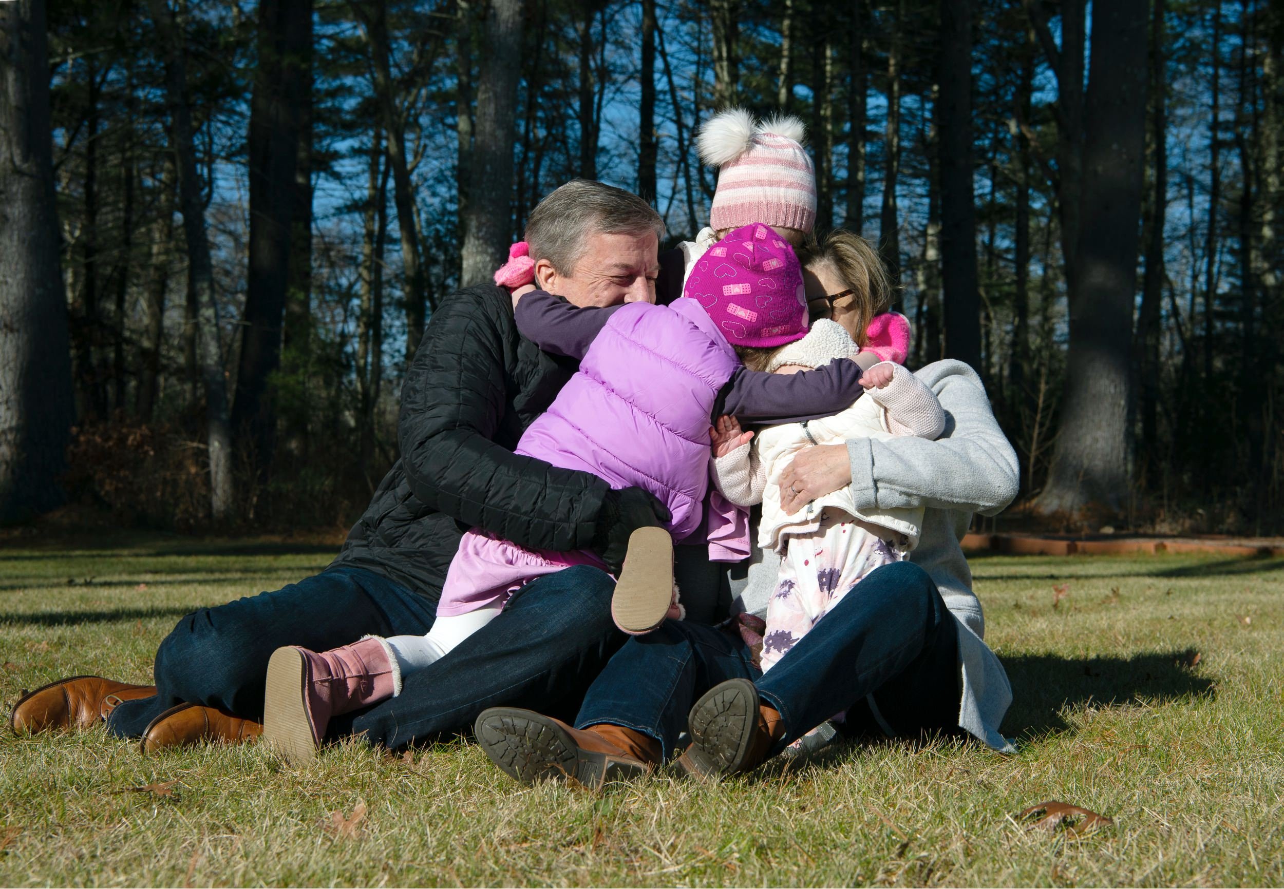 Group hug with grandparents and grandchildren outdoors on the lawn during a winter family session in Rehoboth, MA.