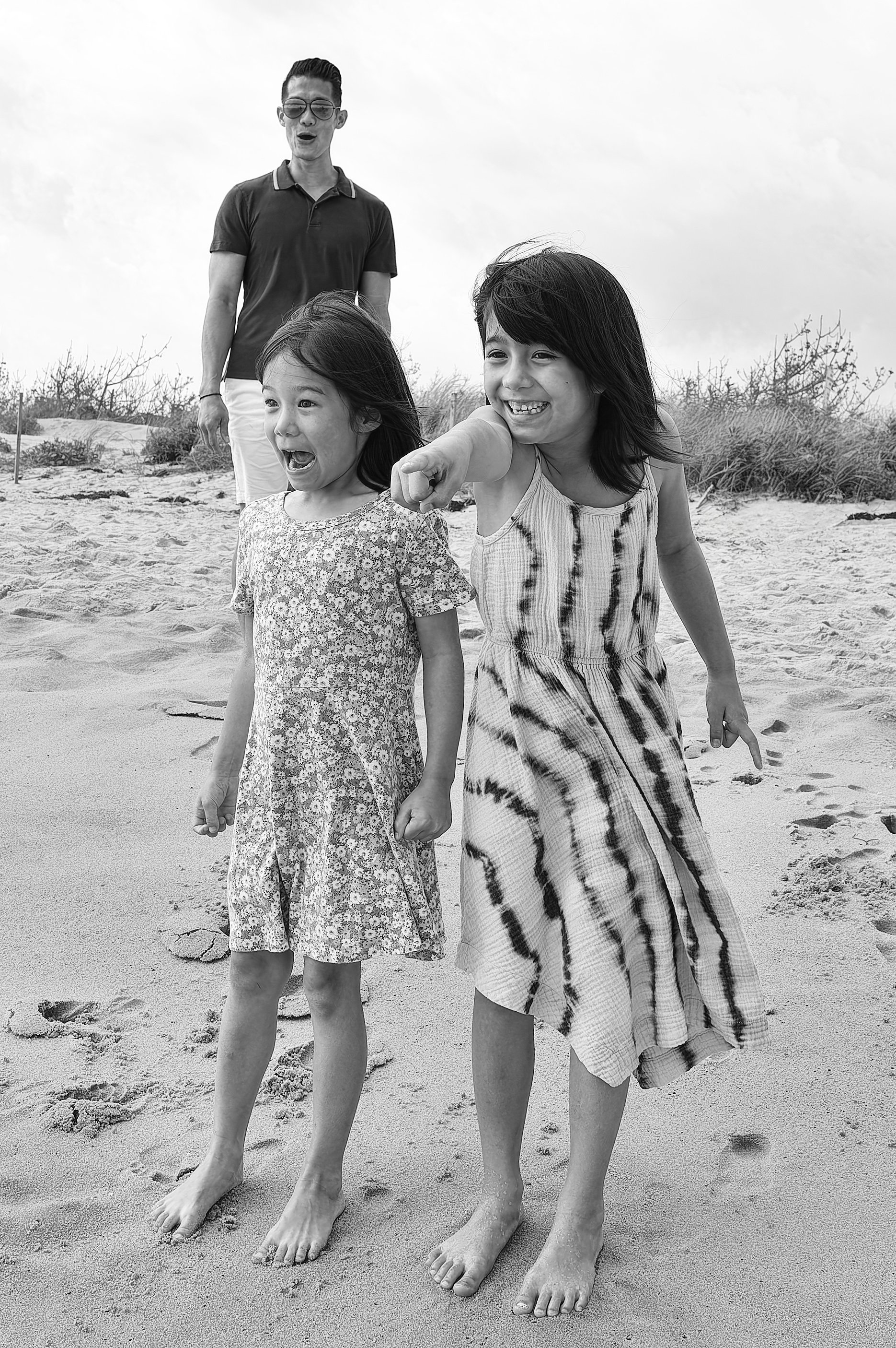 Black and white portrait of two sisters walking together on the beach.