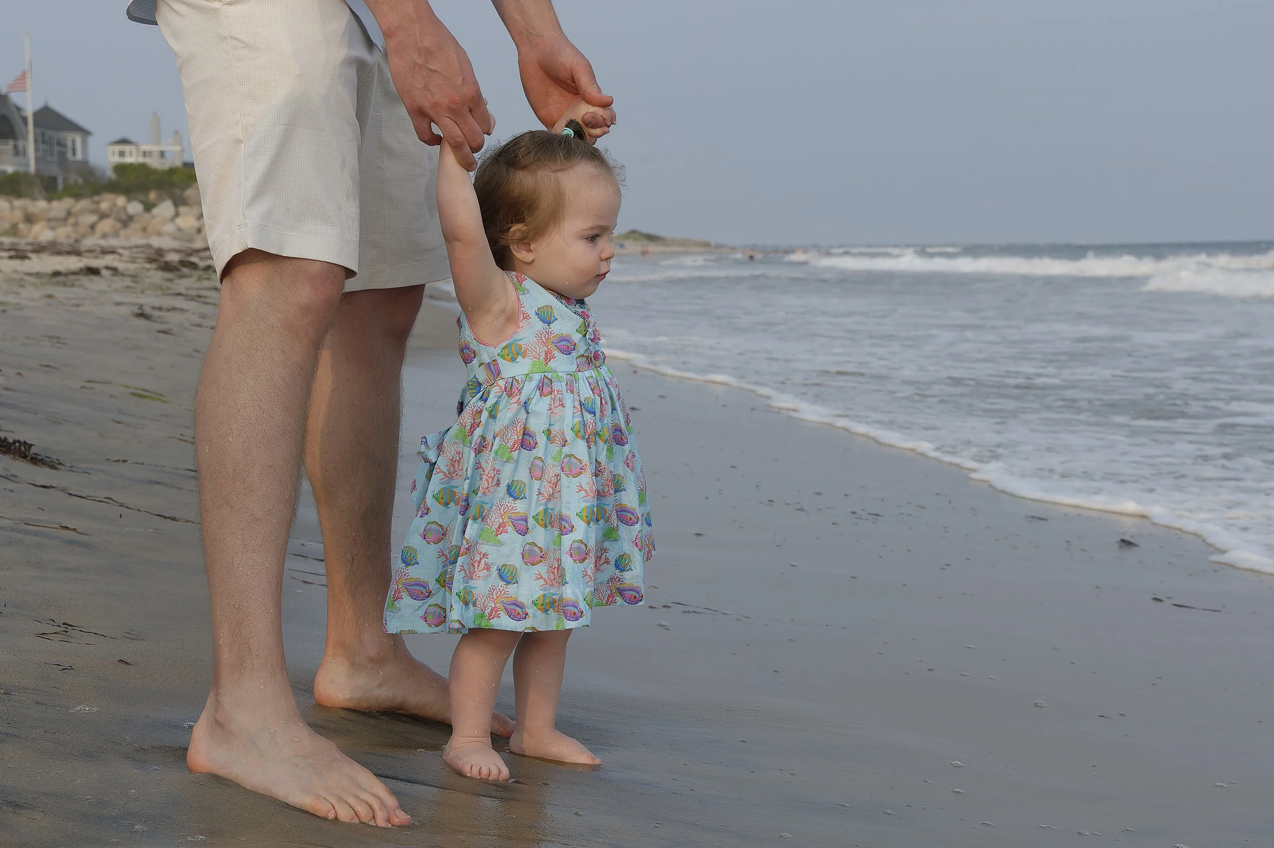 Young girl standing with dad at the water's edge.