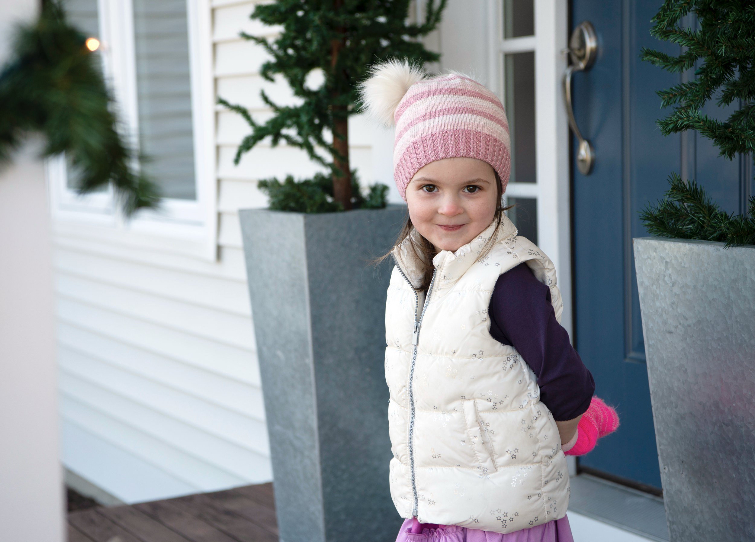 Young girl standing outside in a winter hat and vest during a family portrait session.