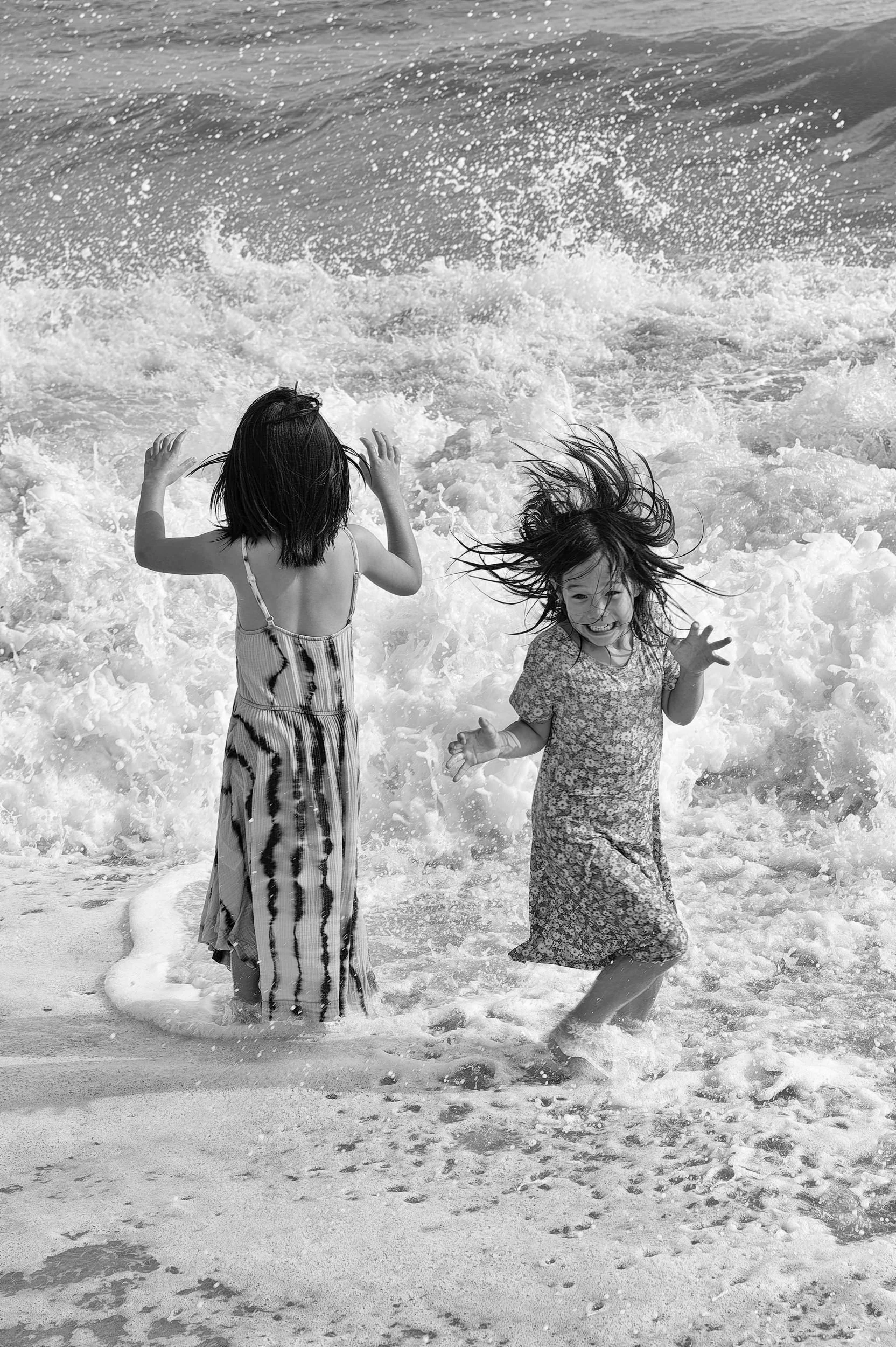 Black and white candid moment of two sisters playing in the water.