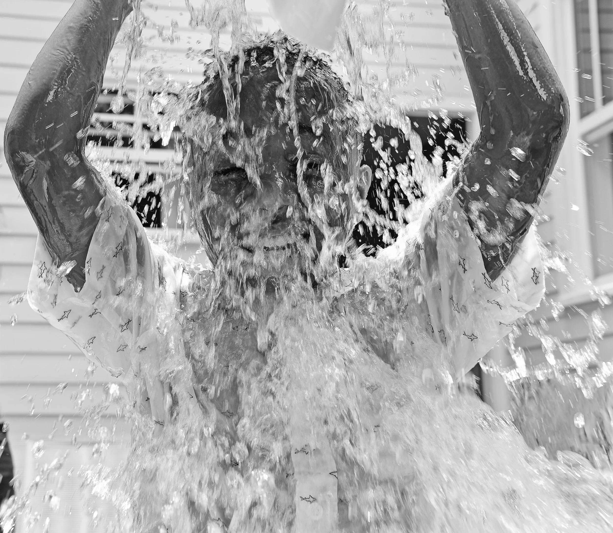 Black and white picture of little boy with big smile as he pours water over his head in a children's pool after a St. Bernard Project ribbon cutting.