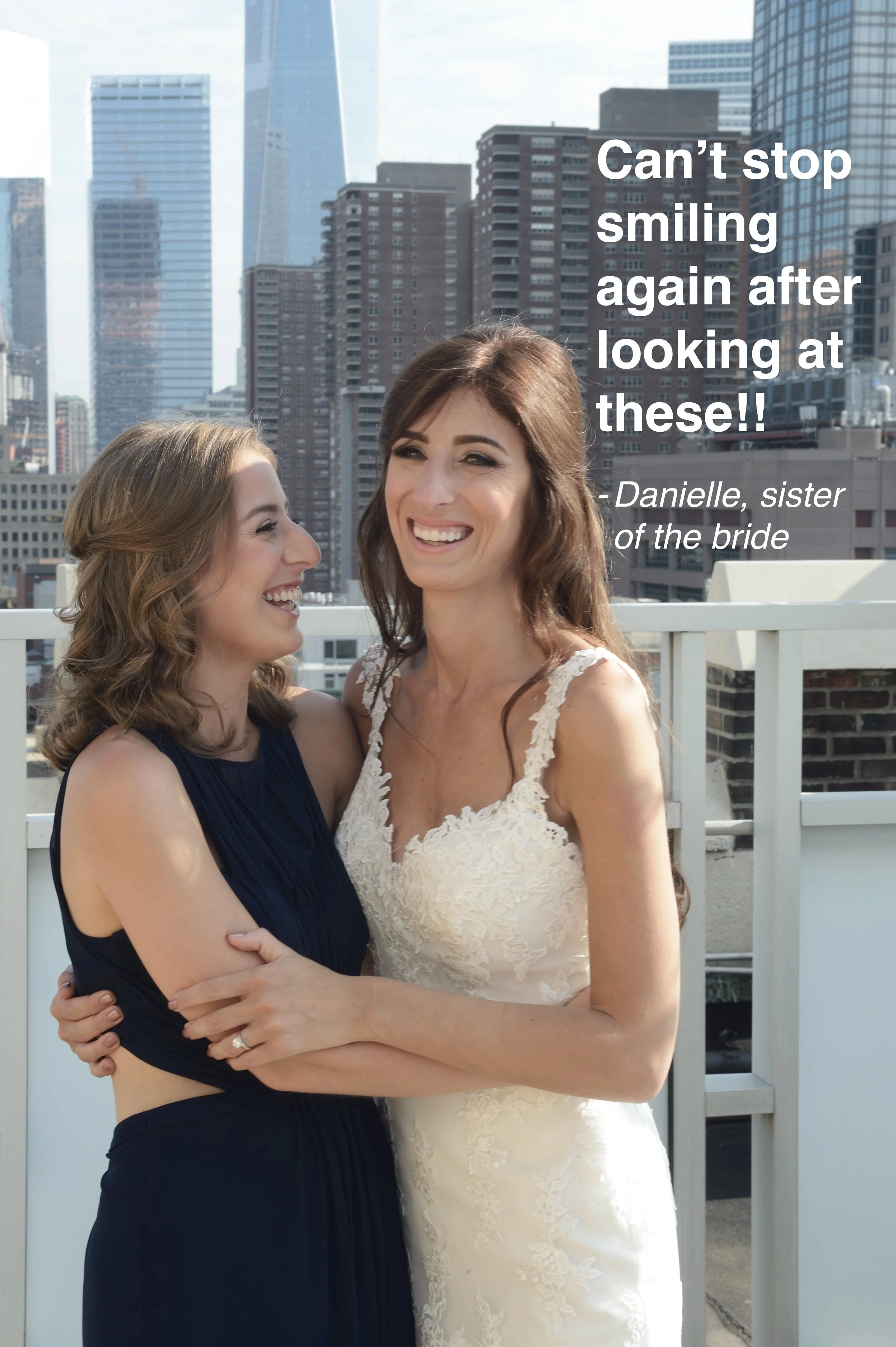 Two women, one in a navy blue dress and the other in a white wedding gown, smiling and embracing on a balcony with a city skyline in the background.