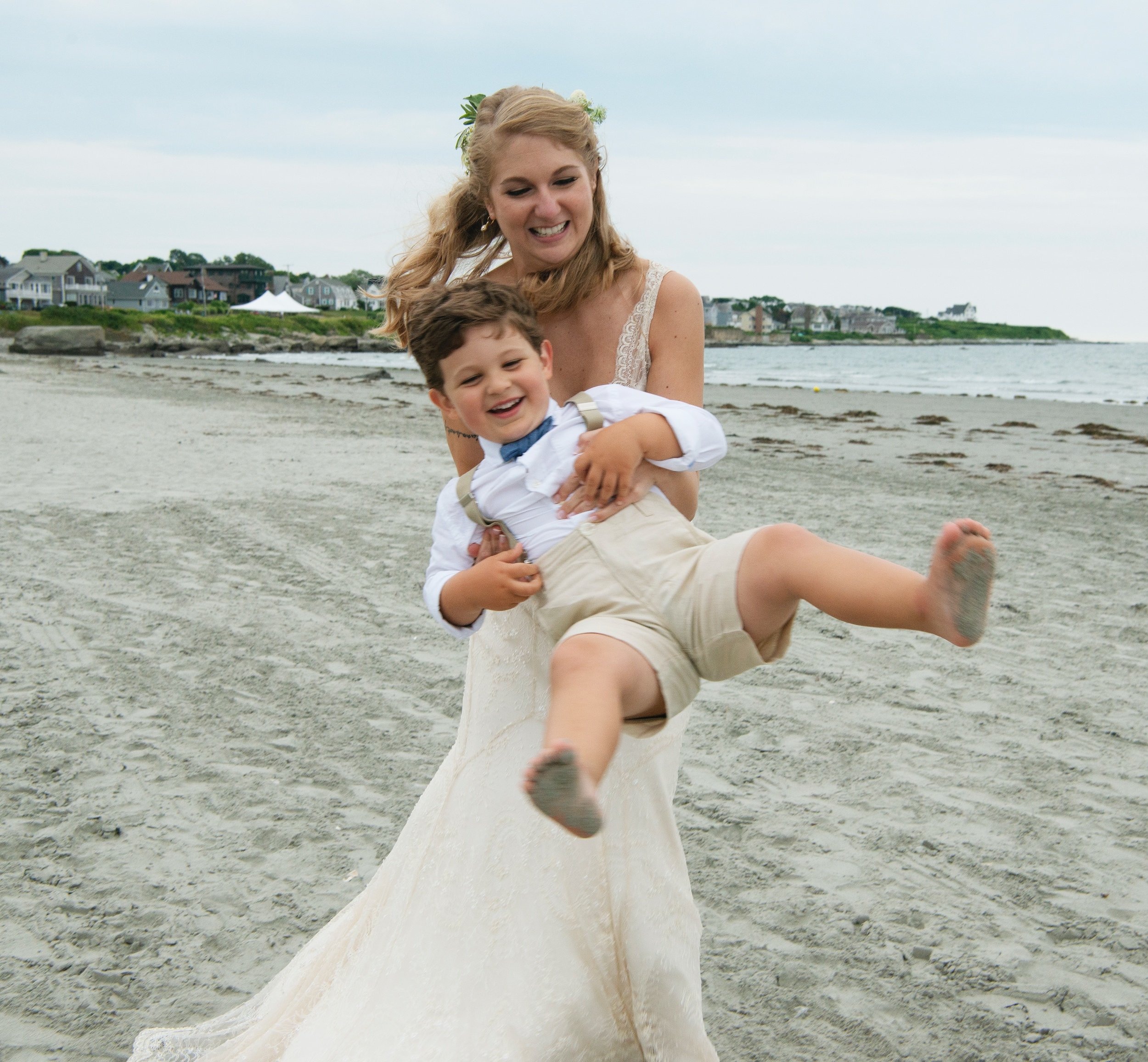 Bride twirling around the young boy ring bearer with his feet flying in the air on the sandy beach