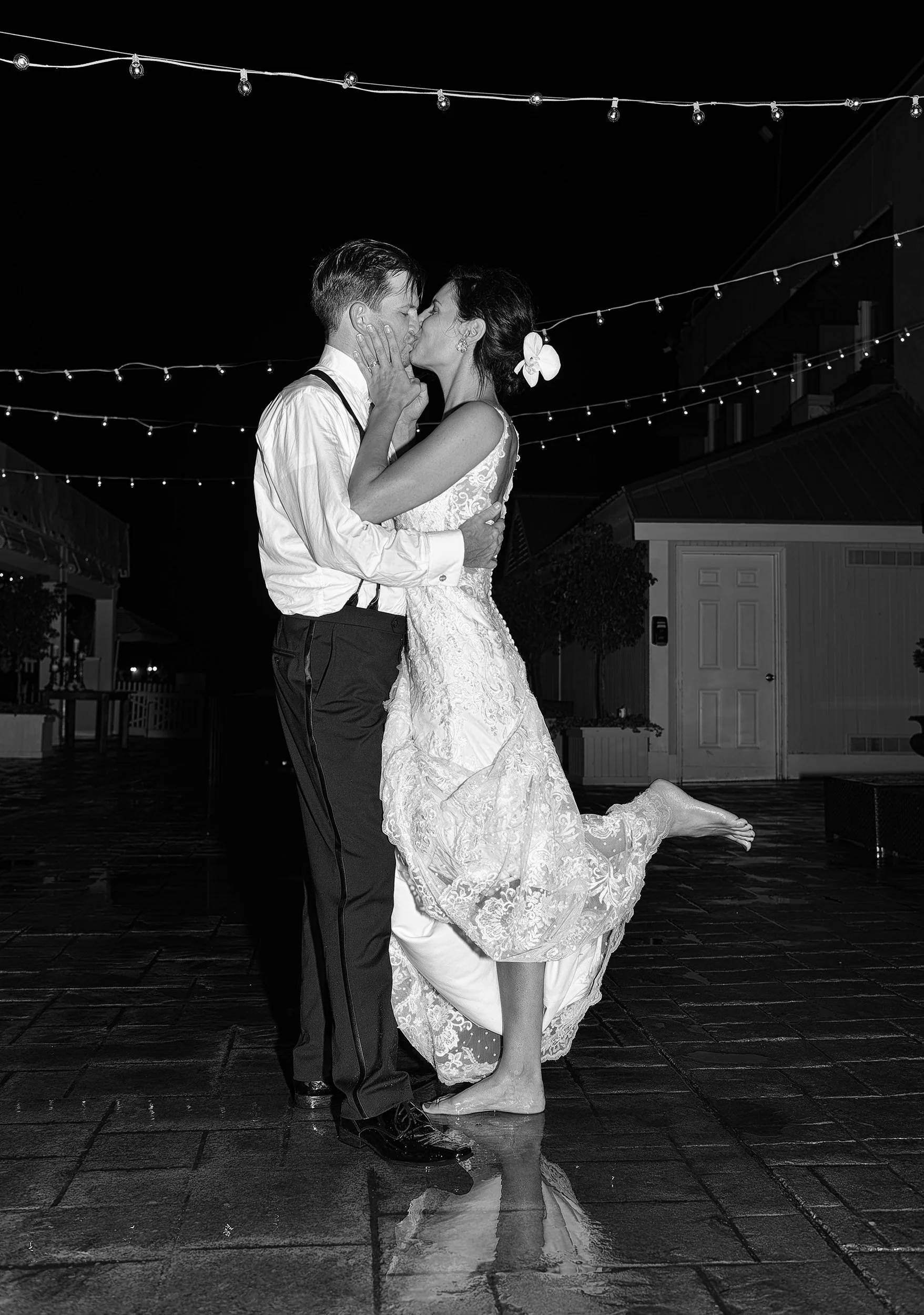 Bride and groom kiss outside with feet in rain puddles at night at Regatta Place