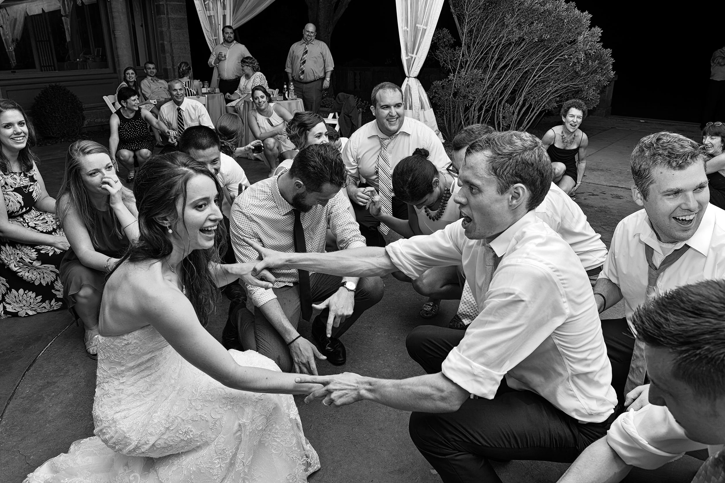 Black and white fun documentary photo of bride and groom dancing with guests around them.
