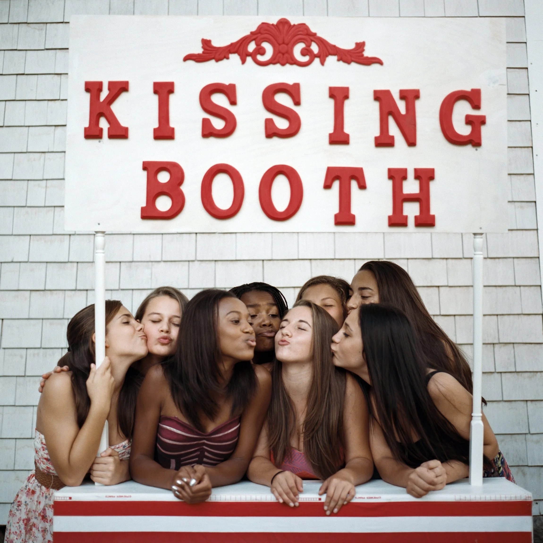 The birthday girl and her friends under kissing booth sign.