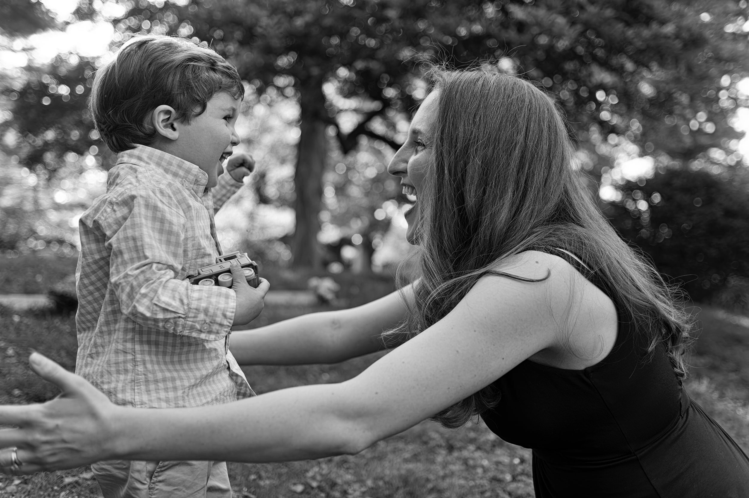 Classic black & white of little boy running into his smiling mothers arms while holding onto his train toy..