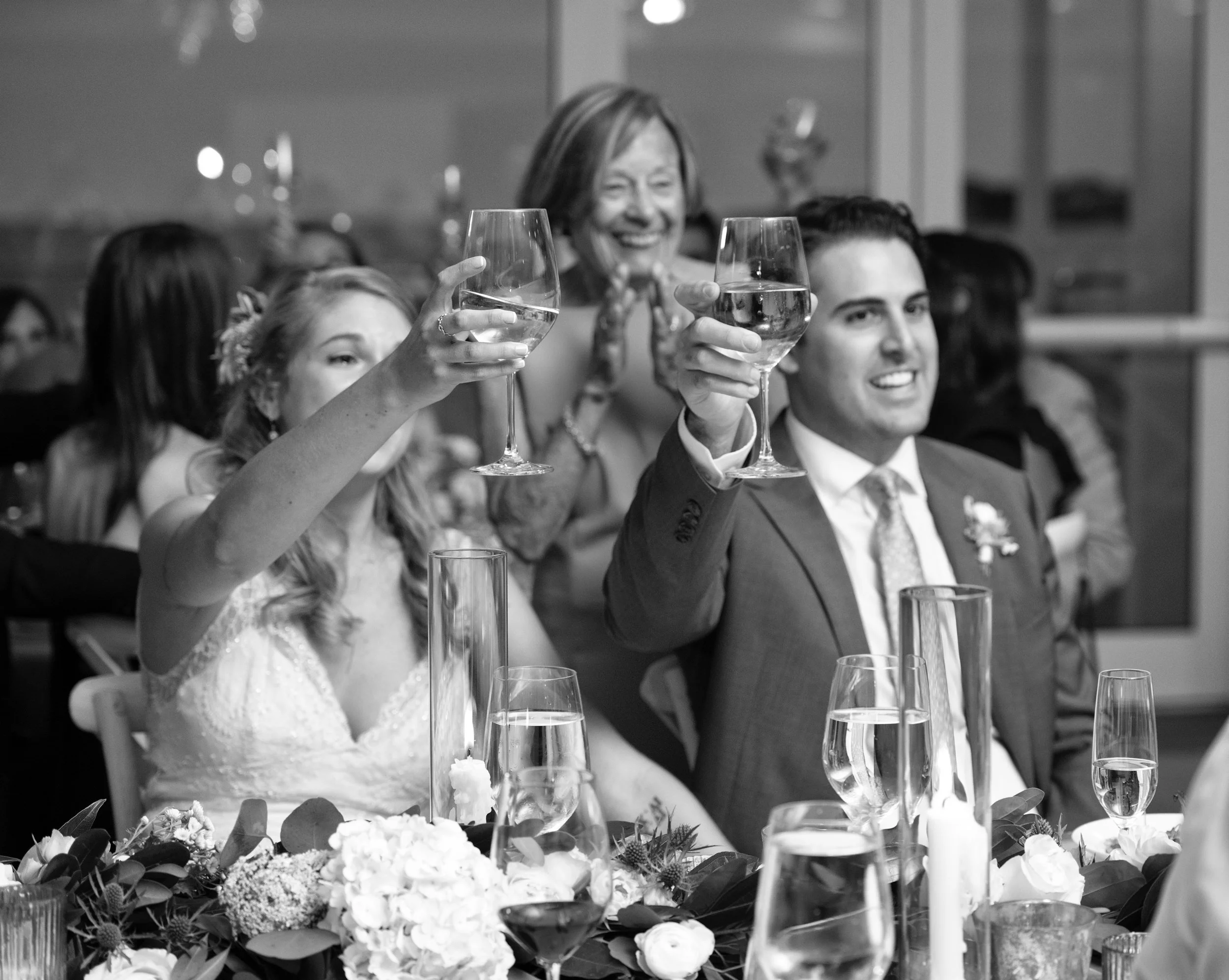 Black and white of bride and groom raising glasses during toasts at Newport reception