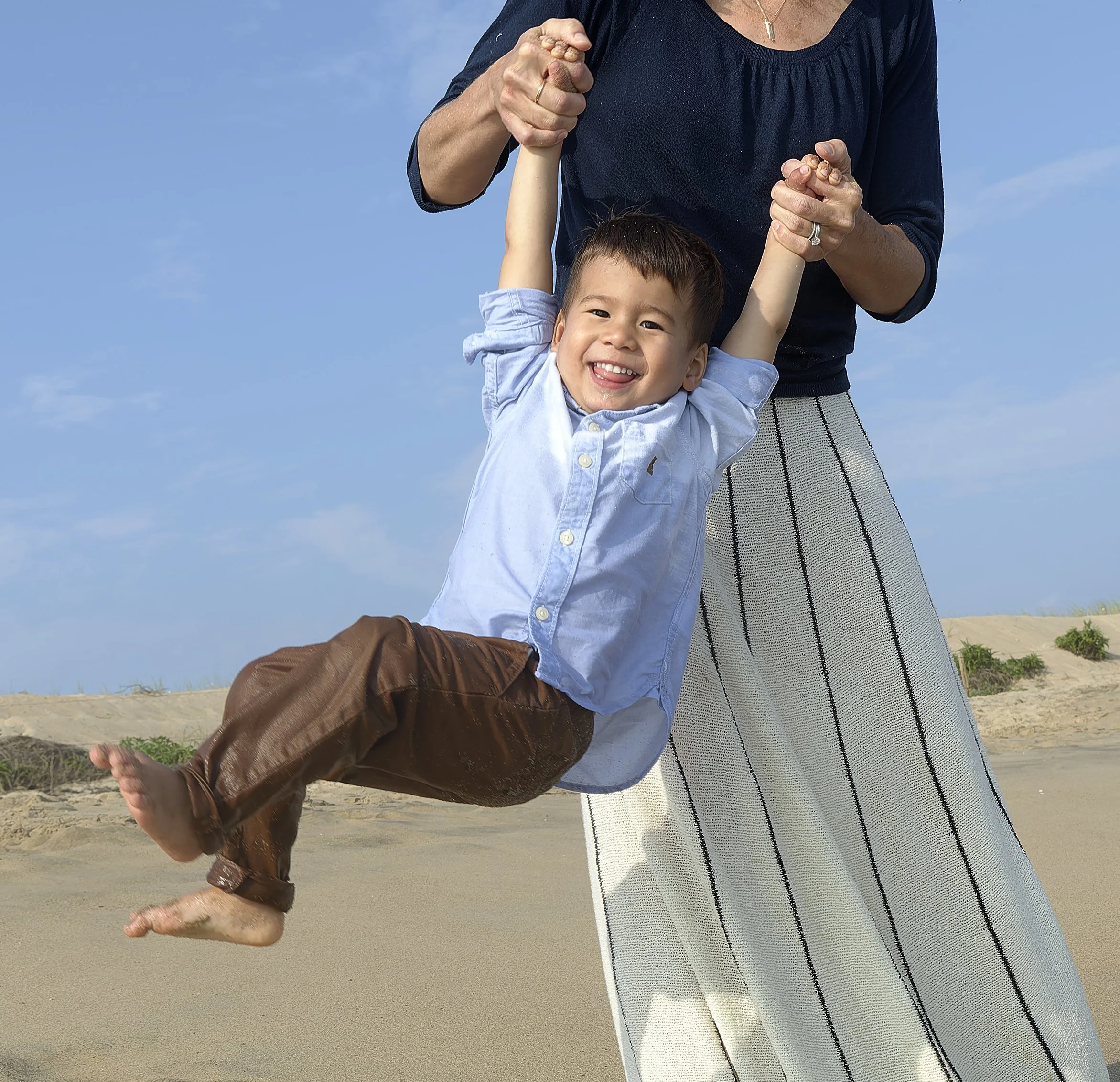 Young boy swings in his mother’s arms with a big smile on a Martha’s Vineyard beach.
