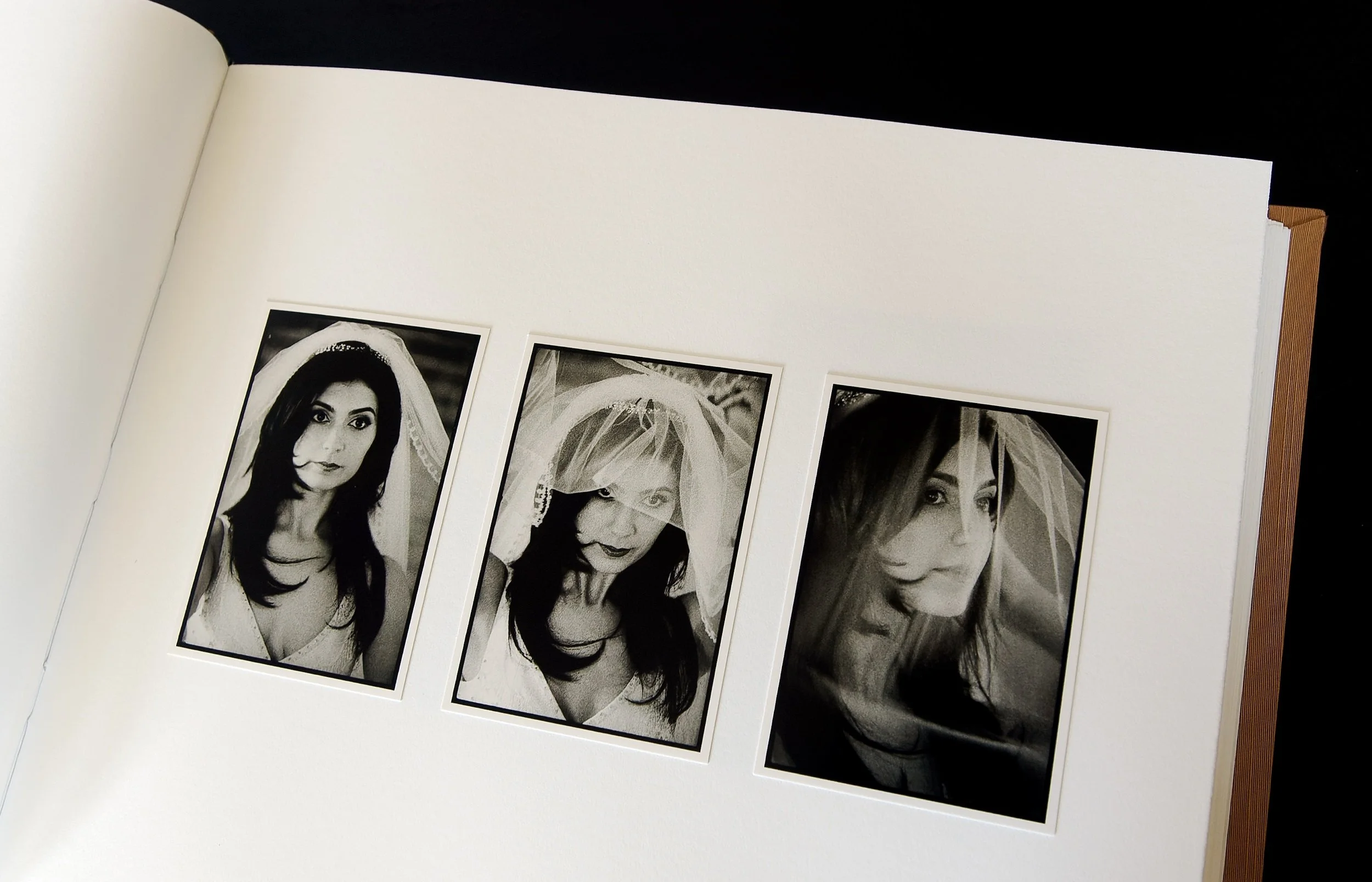 Open album with three candid portraits printed full-frame with black film borders on Ilford black and white fiber-based paper, hand-mounted onto page.