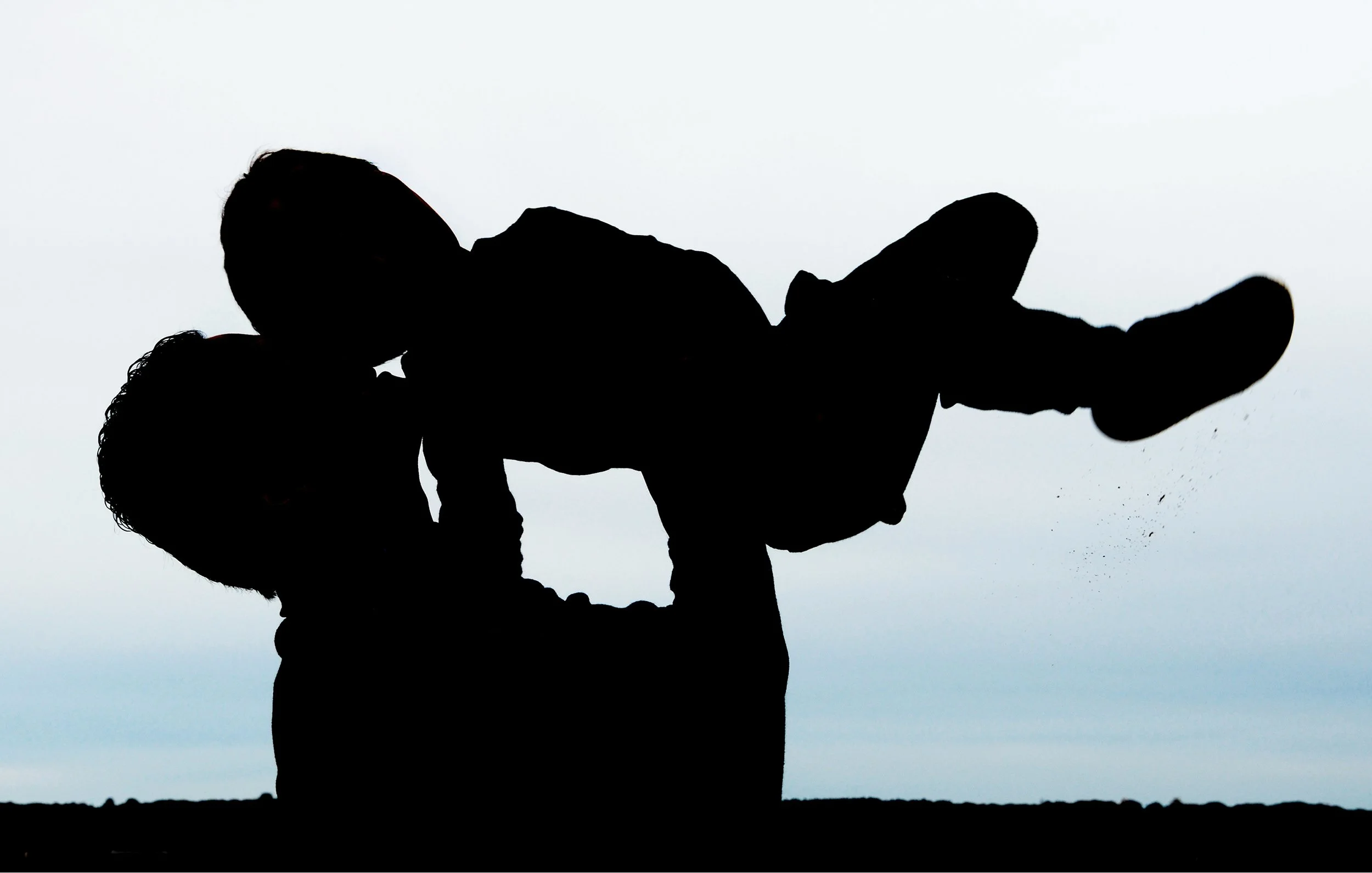 Silhouette photo of father holding young son up in the air displaying love, affection, and energy.