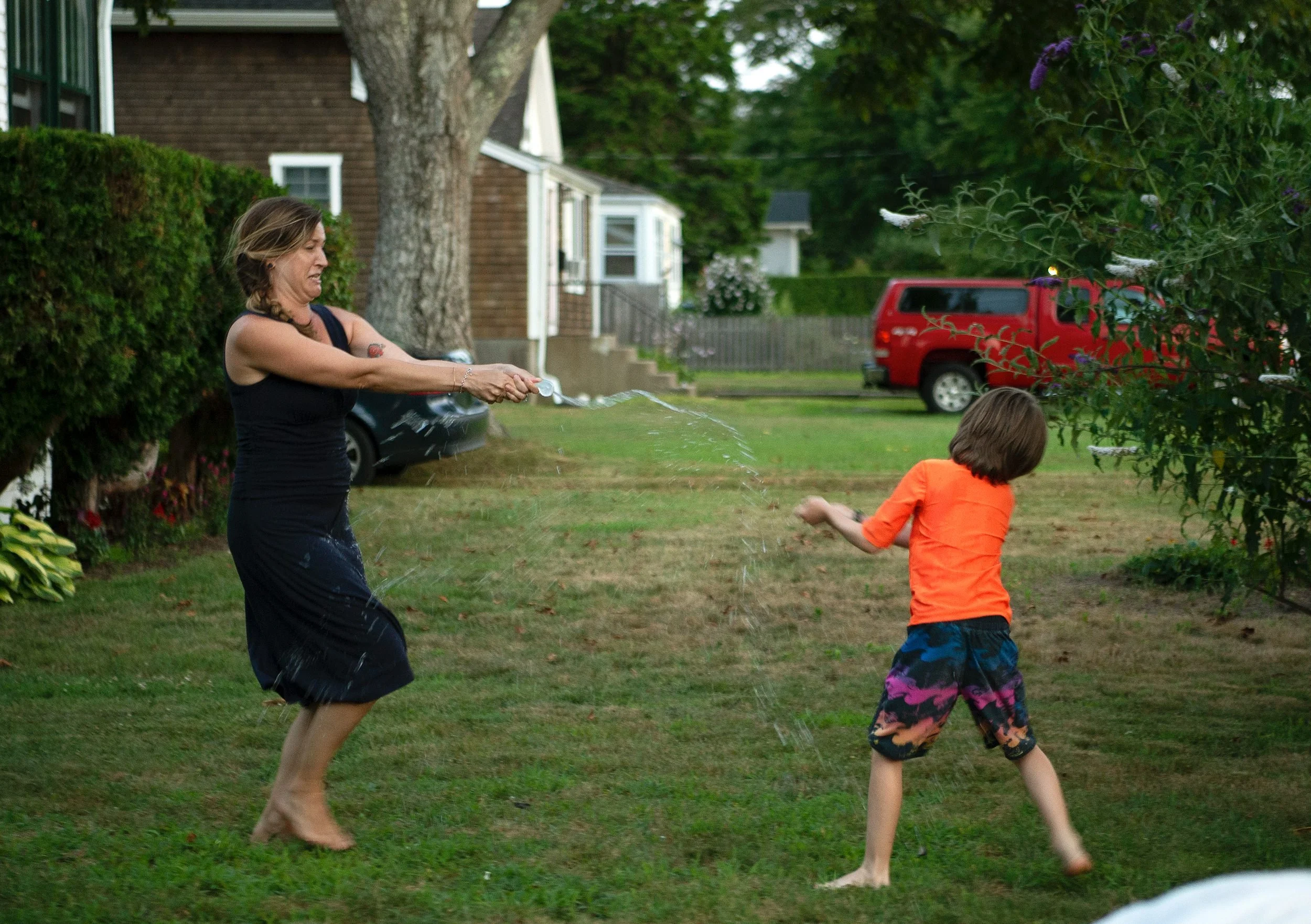 Mother and son playing with water outside on a grassy yard.