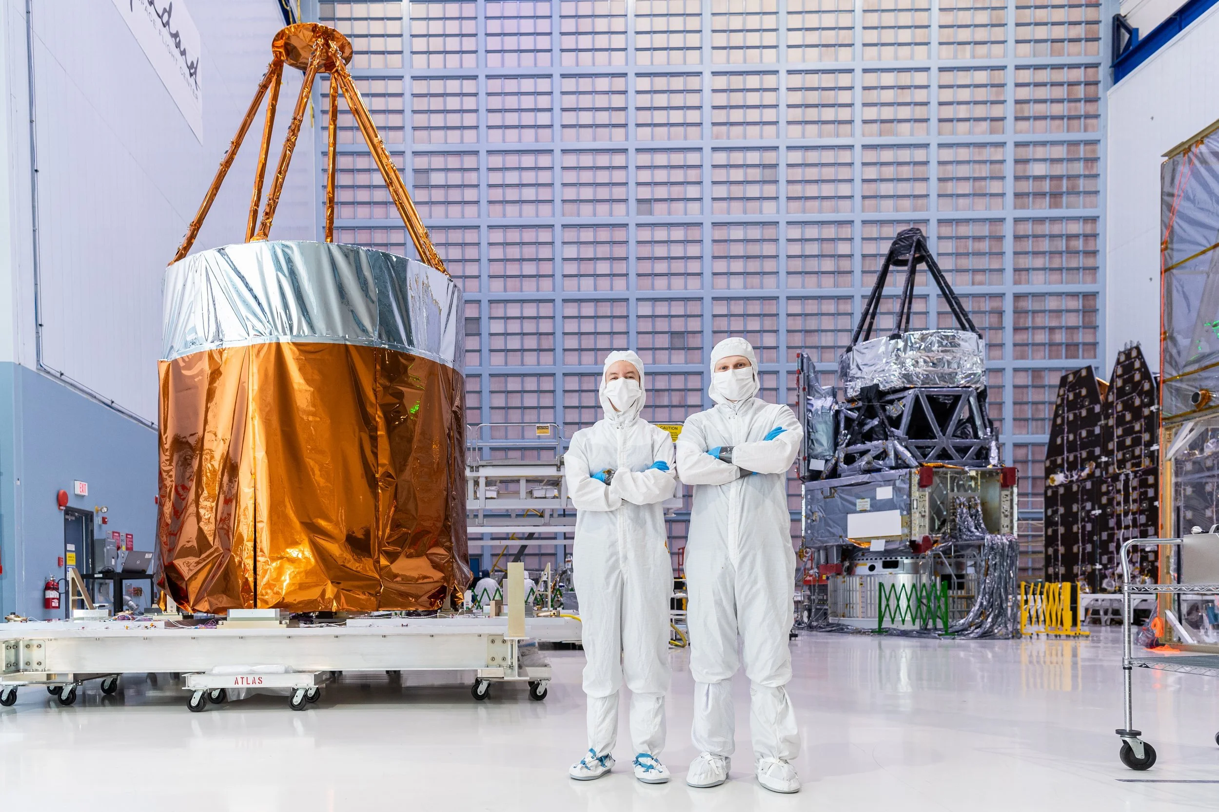 Two engineers in cleanroom suits stand in front of the NANCY GRACE ROMAN Space telescope at Goddard Space Flight Center, Greenbelt Md.,