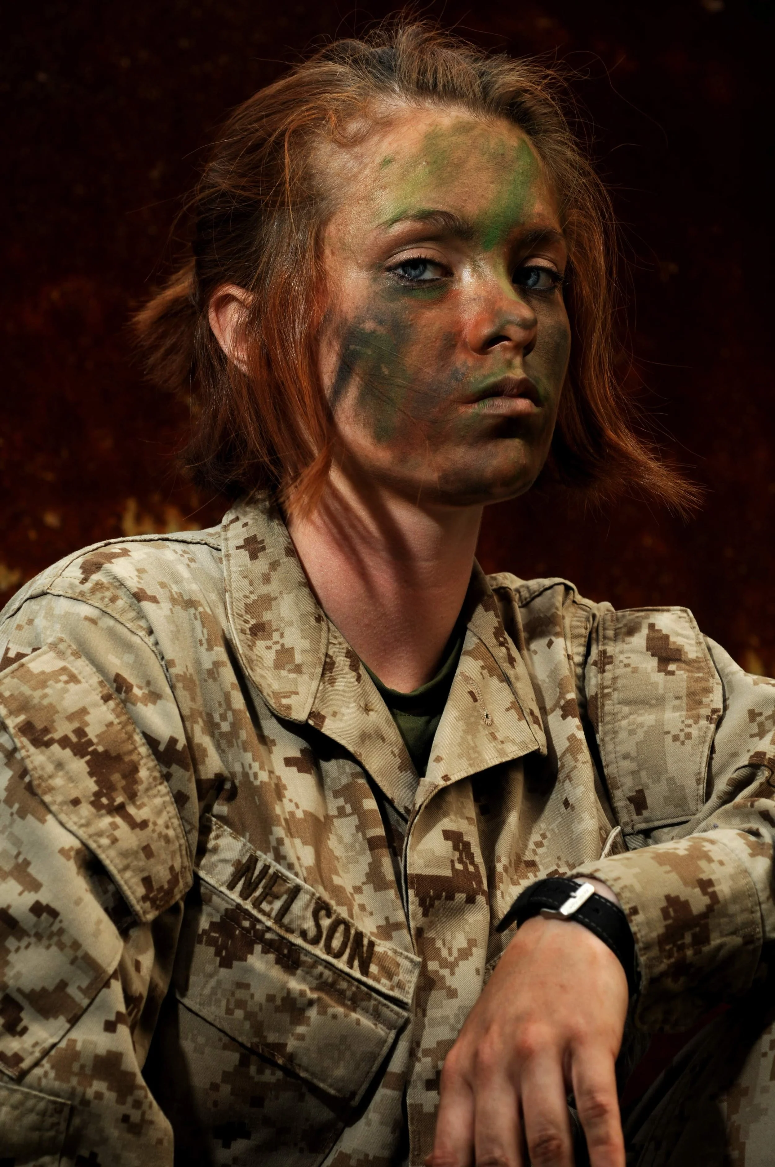 A woman in military uniform with face paint, wearing a watch and sitting with her arm resting on a surface.