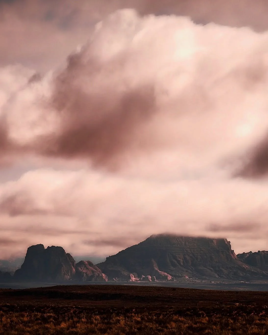 The land rolls out in quiet power beneath a sky stitched with clouds—dramatic, vast, and endlessly ancient. Near Page, Arizona, mesas and buttes rise like sleeping titans wrapped in morning mist, shaped over eons by time, wind, and water. This