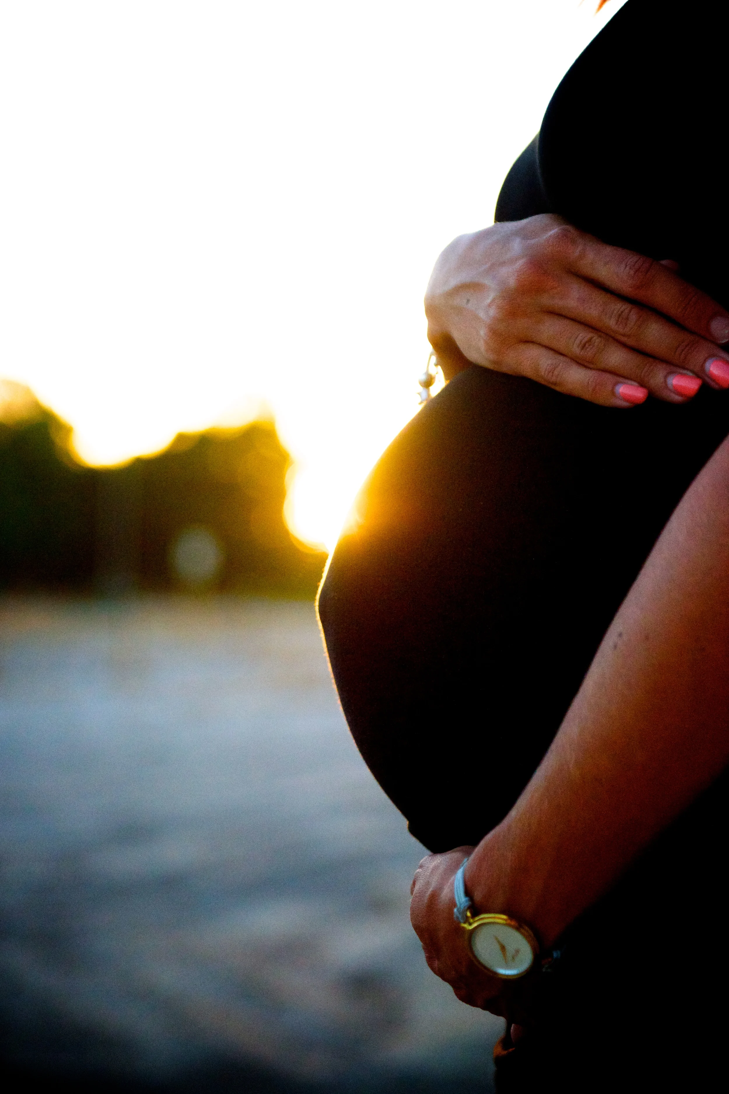 An expecting Mum holds her pregnant belly in front of the setting sun in Perth Western Australia. Image taken by Warnock Imagery