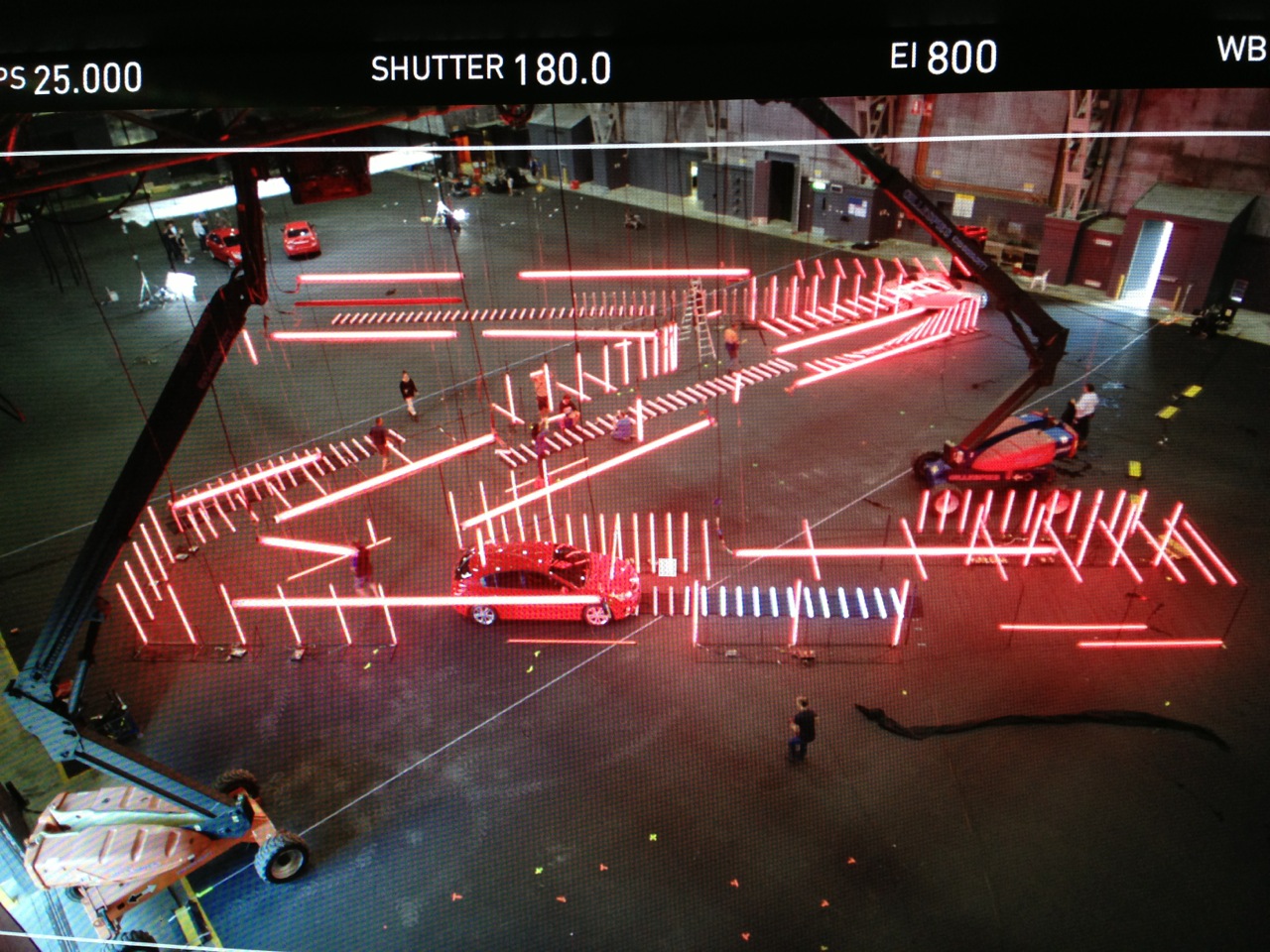 Camera tape on studio floor indicates set out positions of lighting hanging from ceiling grid in extreme foreground