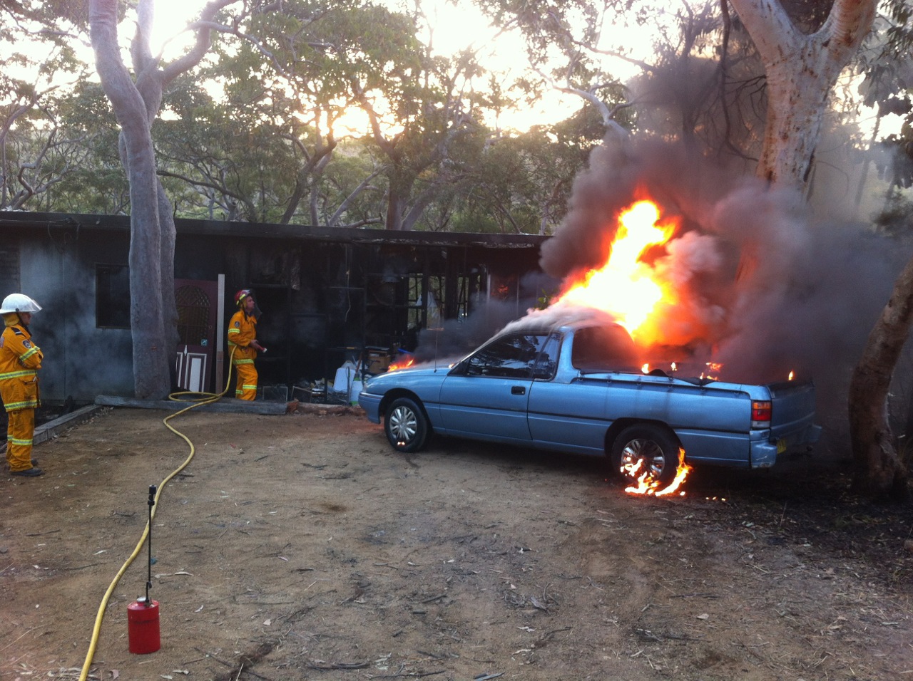 Burning car with rural bush fire volunteers