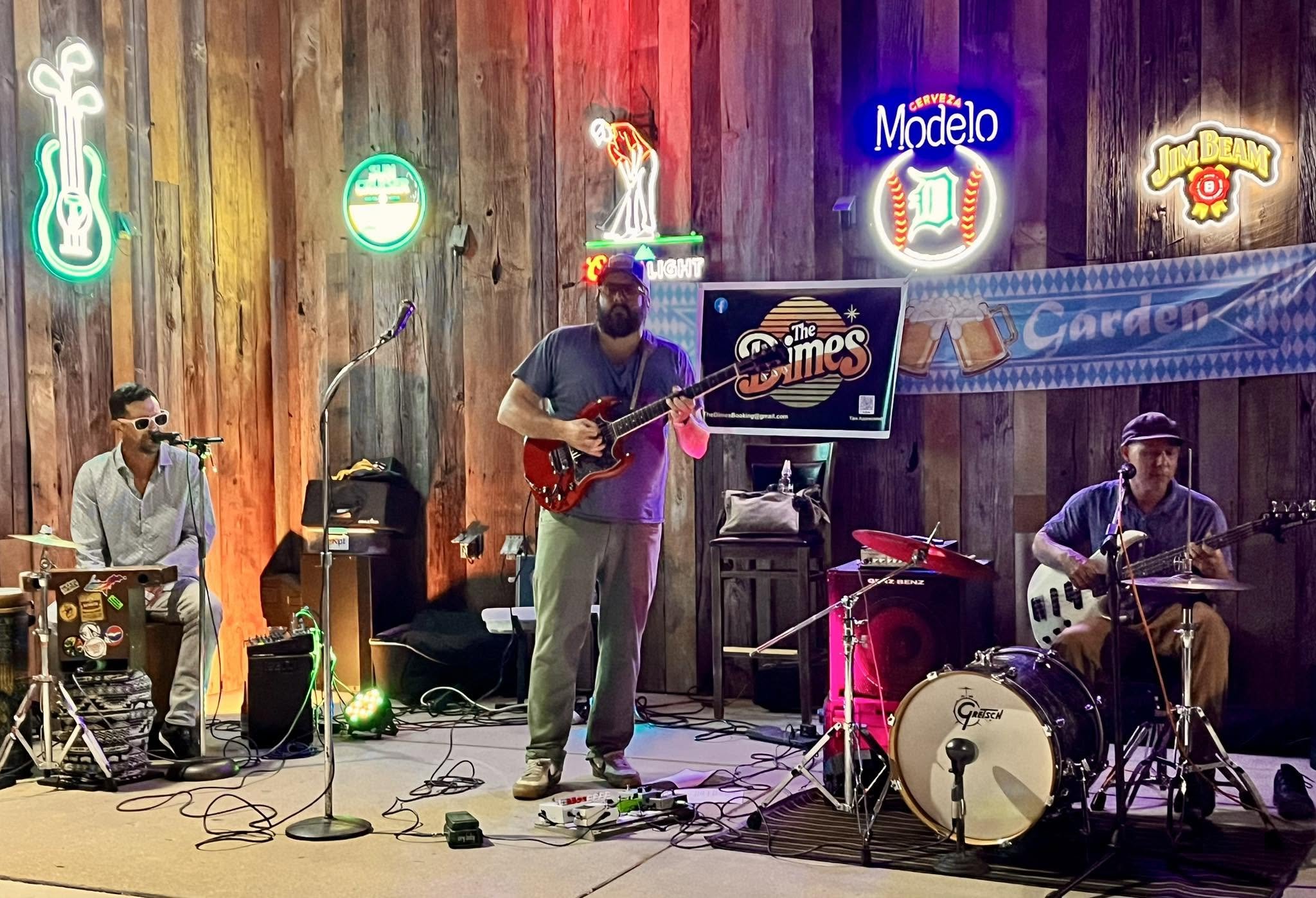 The Dimes play in front of a wall with colorful neon signs.