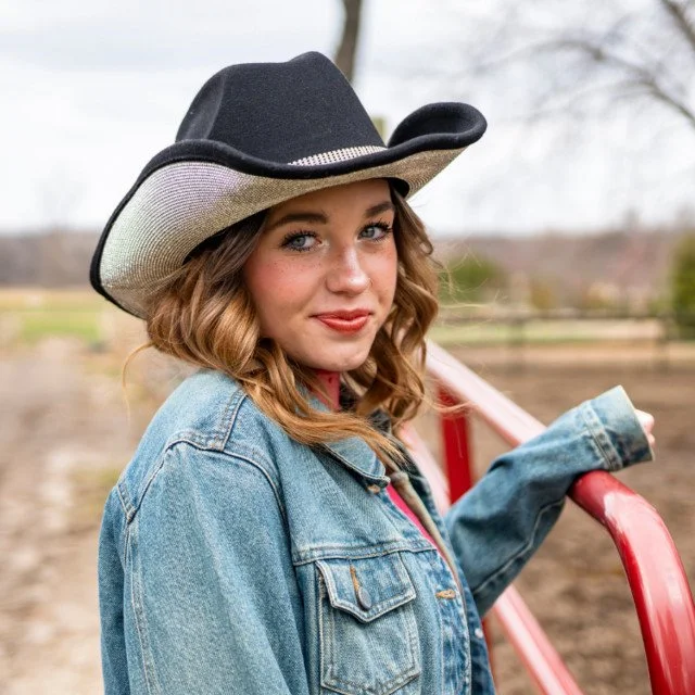 A photo of Jadyn Savage standing against a fence with a cowboy hat.