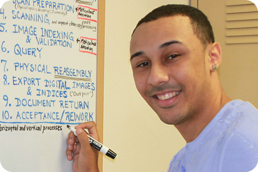 Male student writing on the board and smiling at the camera.