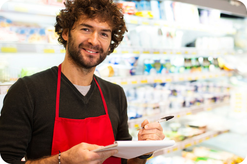 Male with a notepad and pen wearing a red apron and working in a supermarket.