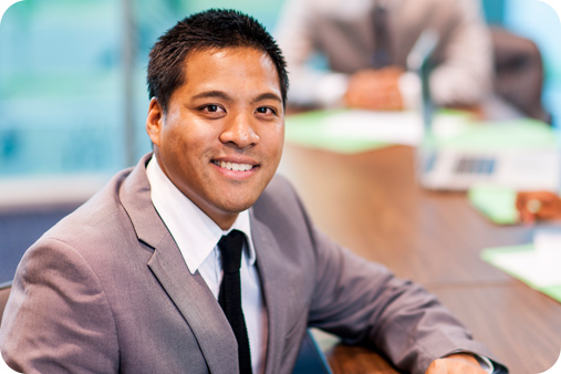 Man wearing a corporate suit in a board meeting smiling at the camera.