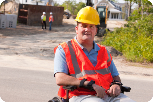 Man on a wheelchair wearing his construction uniform and hat at a construction site