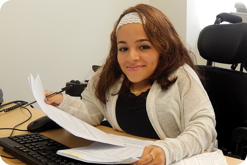 Woman on a wheelchair doing office work and smiling at the camera.
