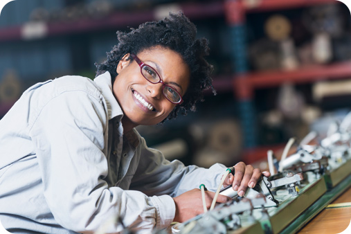 Women wearing glasses and smiling while leaning over some mechanical work she is completing.
