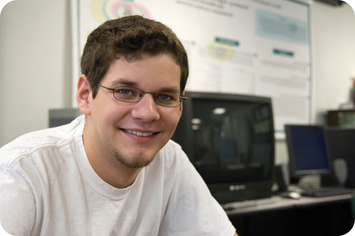 Male student in glasses sitting down and smiling.