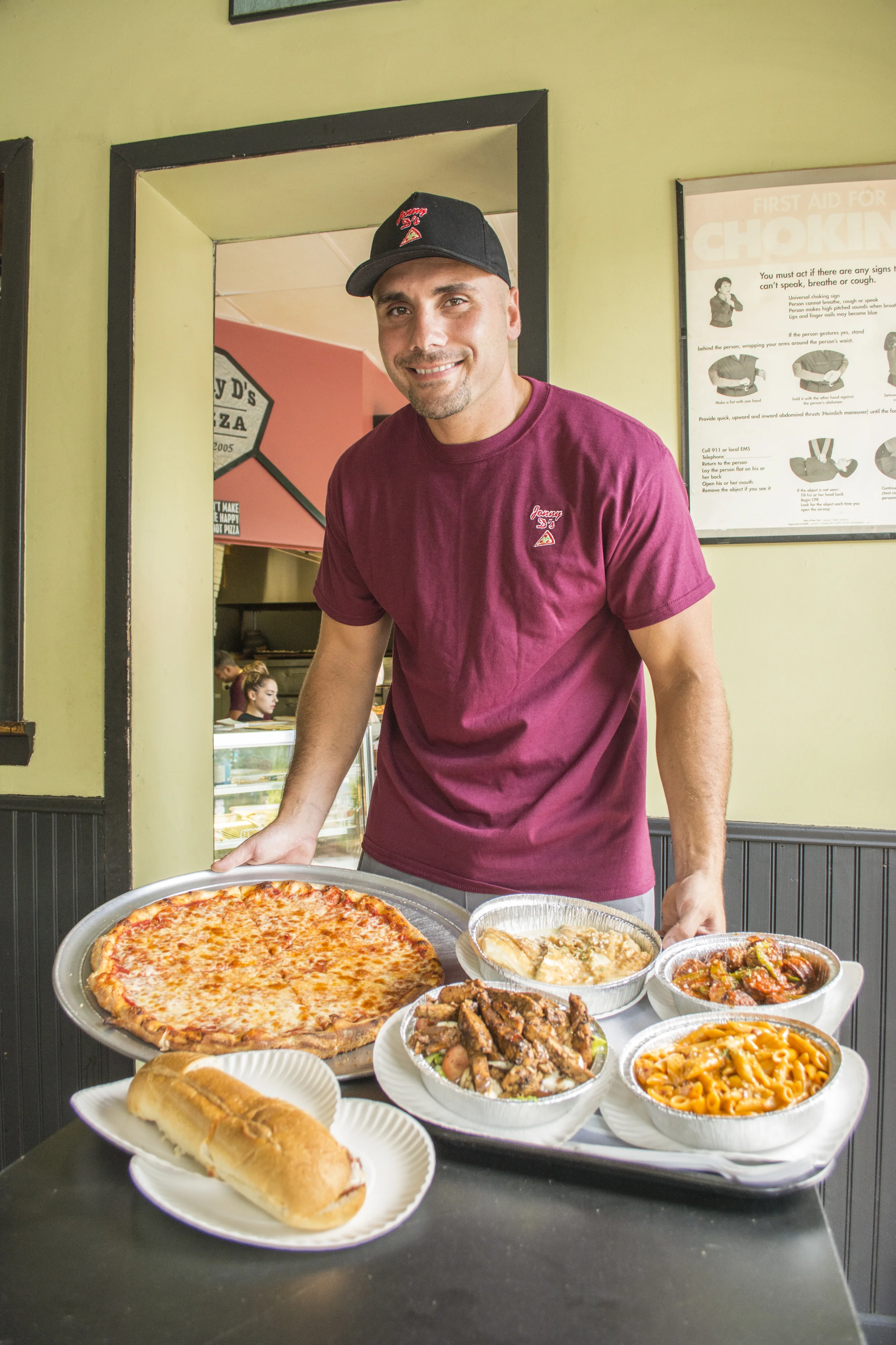 Jonny Dawson, owner of Jonny D’s Pizza, shows off some of the pizzeria’s offerings. From left: a regular cheese pie; chicken parmesan hero; salad with grilled chicken; chicken francese; penne ala vodka; and sausage and peppers.