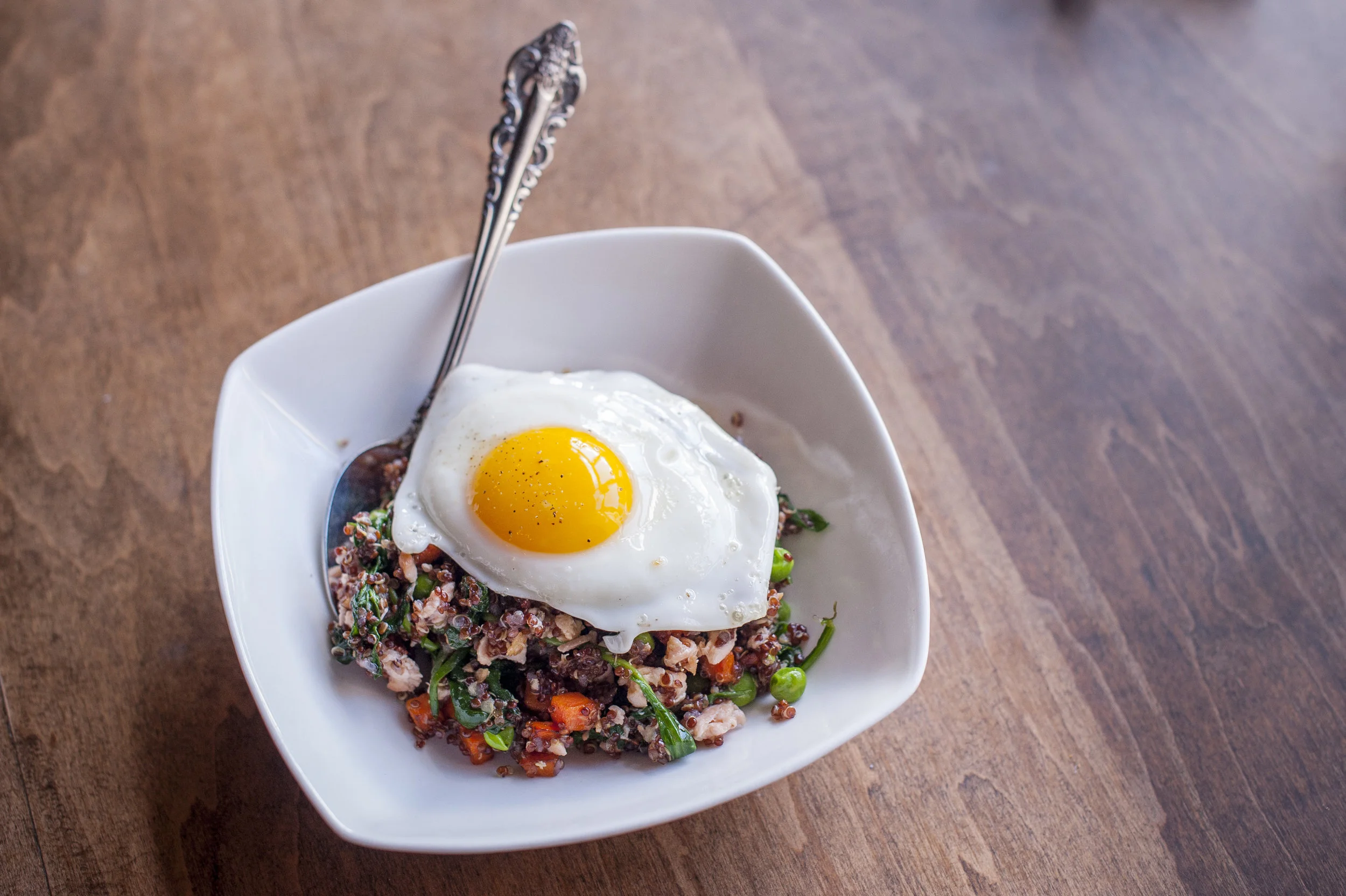 Skip the takeout fried rice and opt for the healthier and even tastier “Fried” Quinoa adorned with peas, carrots and spinach centered around wild salmon all topped with a sunny side up egg.