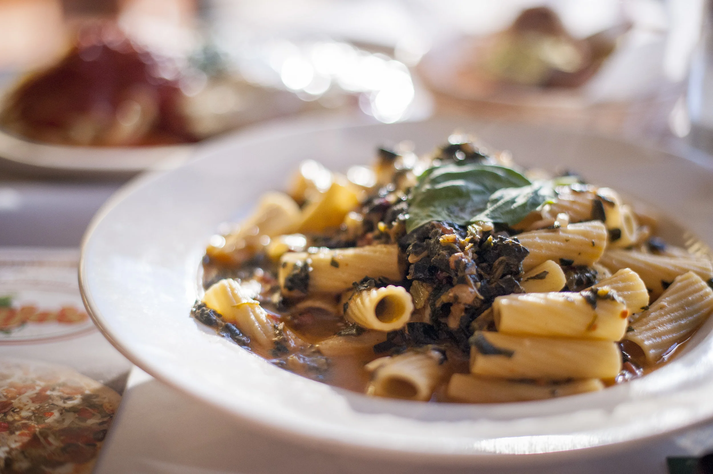 Rigatoni Alla Viajo’s plates a chewy rigatoni pasta in a pomodoro white wine sauce with onions, raisins, spinach and pigtail nuts, coming together to marry the worlds of sweet, savory and nutty.