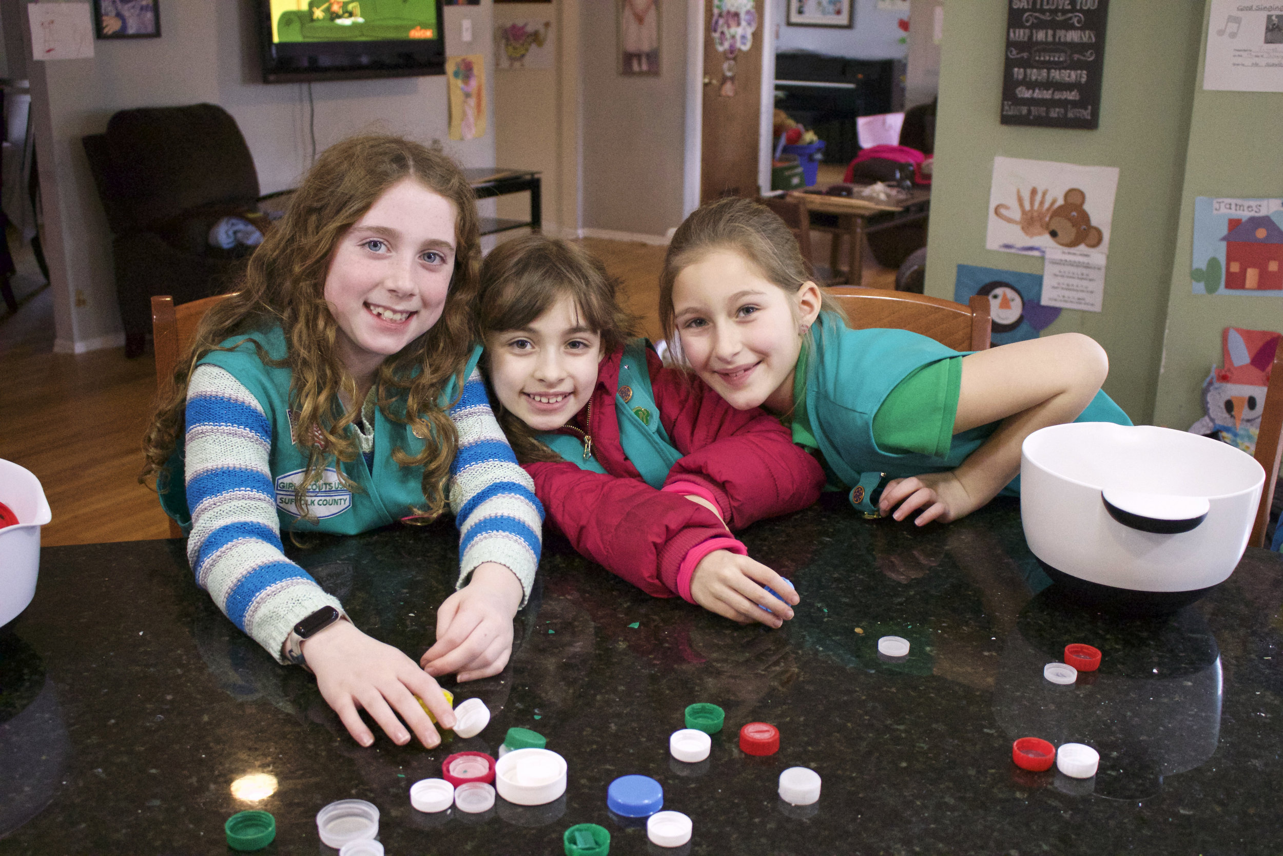  Kate Adams, 9, Leah Linsner, 9, and Lilly Fleischer, 9, are all smiles Saturday while they sift through pounds of plastic caps and lids. 