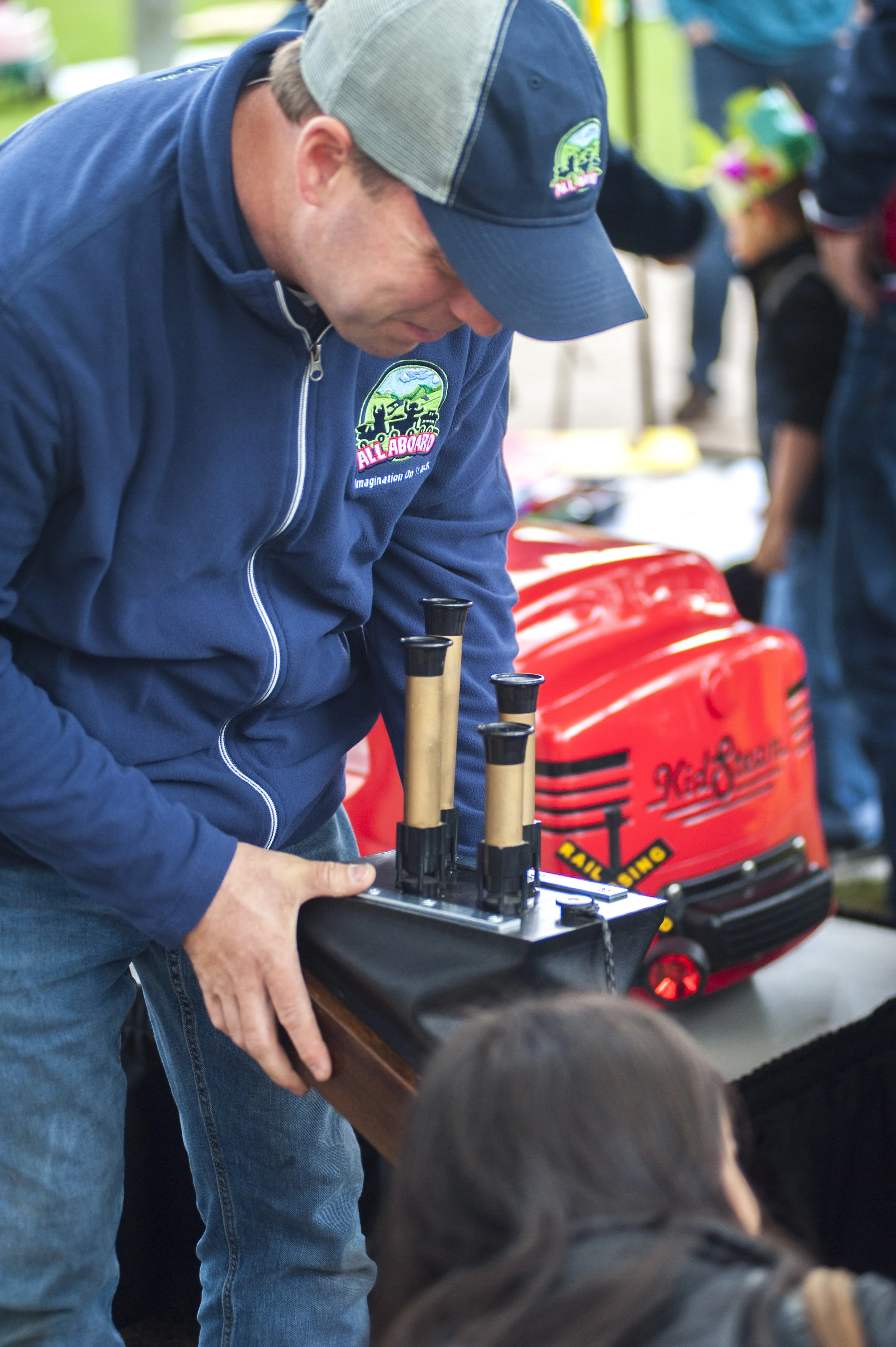  A representative from All Aboard: Imagination at Work, a company that provides kid-powered locomotives and model trains for events and parties, blows the horn of one of the train chimes on display before handing it off to a young boy for a turn. 