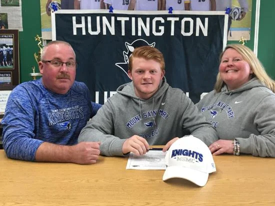   Colby Martin, center, inks his commitment to Mount Saint Mary College in upstate Newburgh.&nbsp;  Photo Courtesy of Huntington Village Lacrosse Club  