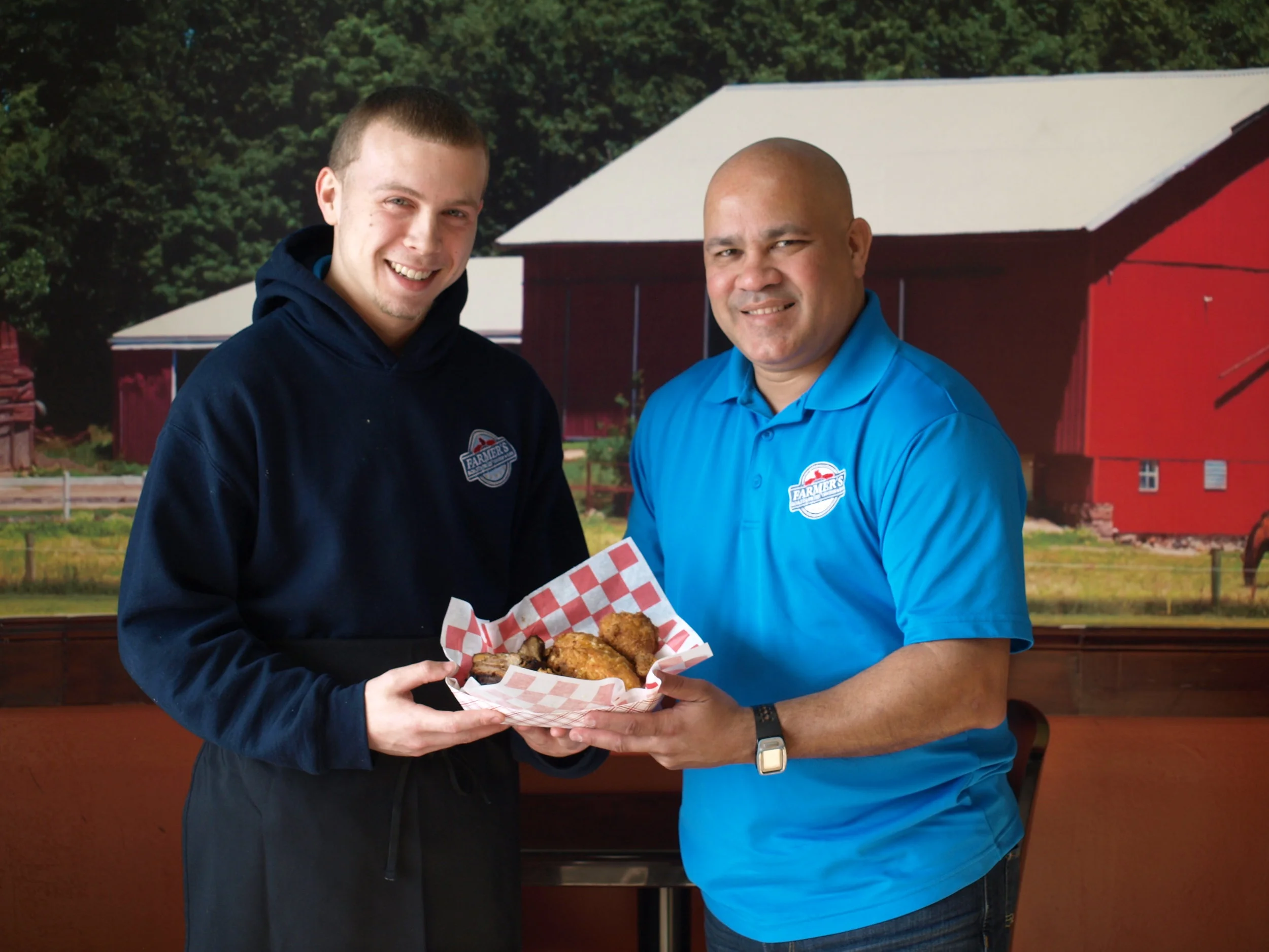   Managing partner at Farmer’s Roastafried Angelo Gonzalez, right, and chief Travis hold a basket of freshly-cooked chicken.   Long Islander New photos/Connor Beach  