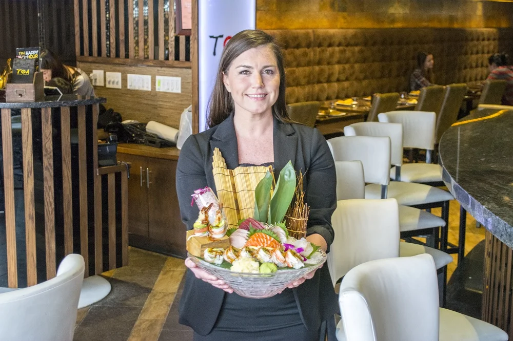   General manager Katie Moore, of Huntington, said the quality of food is what sets T.O.A. apart. She’s presenting the restaurant’s artfully plated Sushi and Sashimi Combo ($30).   (Long Islander News photos/Connor Beach)  