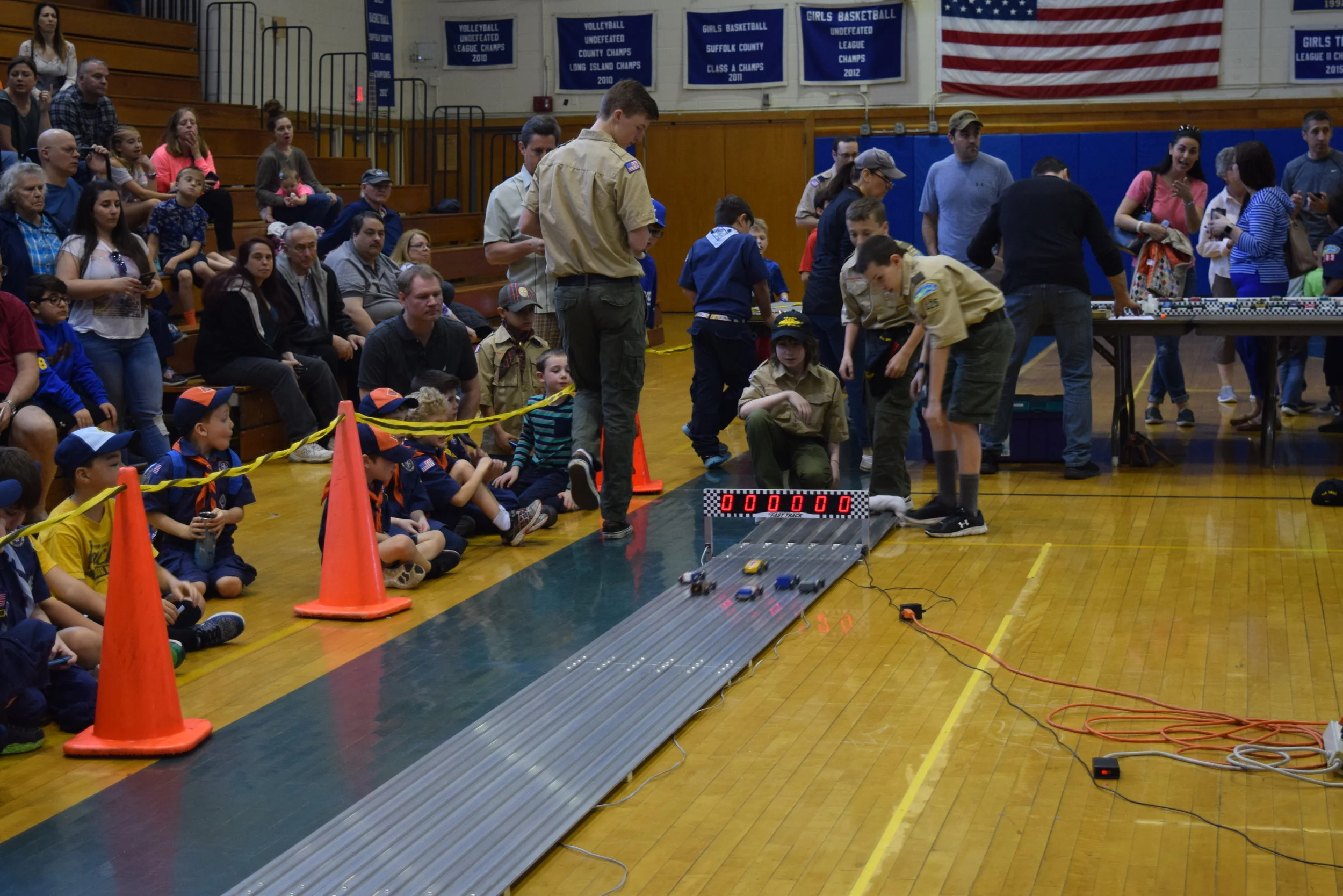   Cub Scouts and their parents watch the racecars as they near the end of the runway and the “pit crew” Boy Scouts get ready to retrieve the cars at the end of the track.  