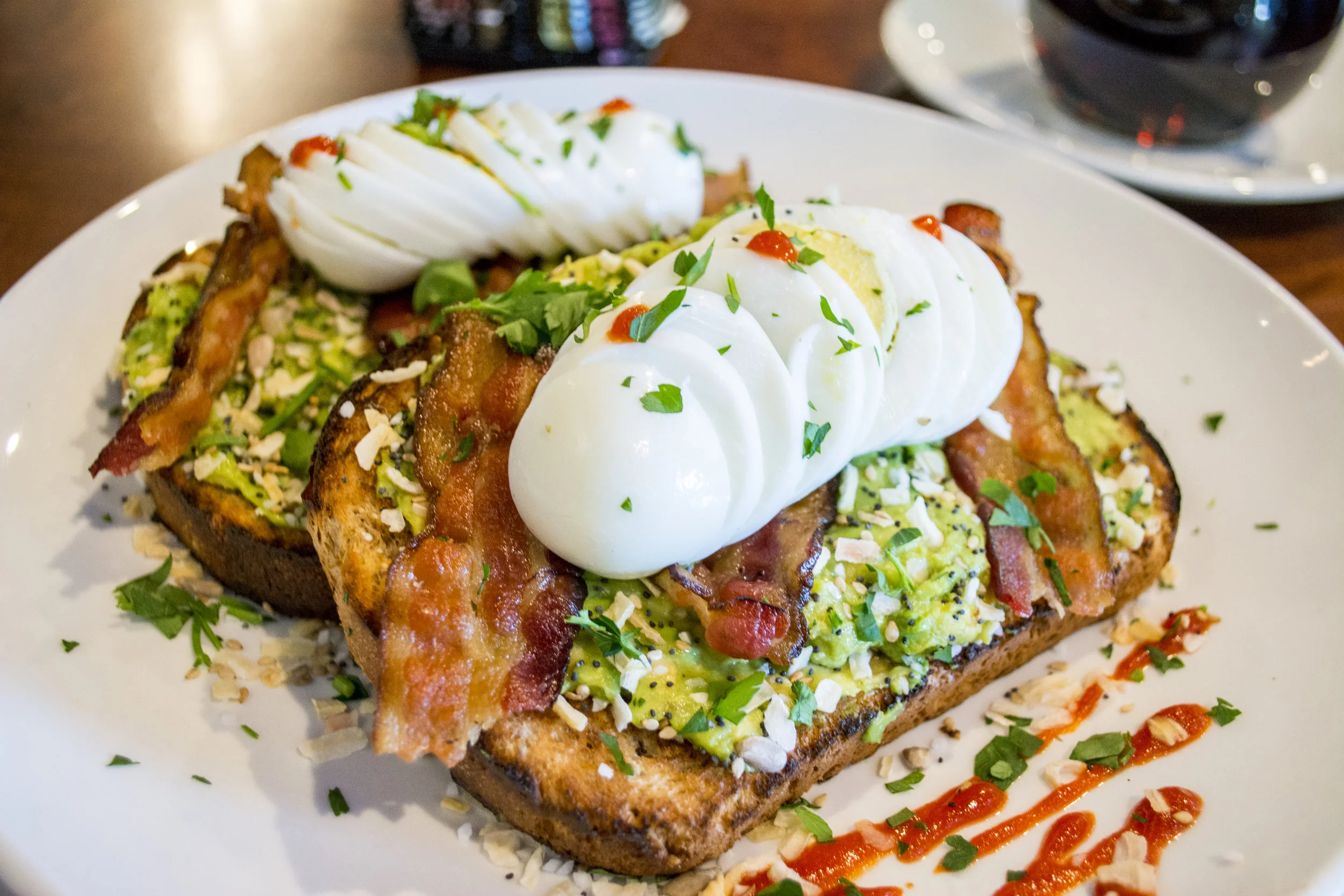   Everything Seed Bacon Sriracha Avocado Toast ($12.99) includes fresh avocado spread, bacon, sliced hard boiled eggs, everything bagel seeds mix and Sriracha on multigrain toast.  