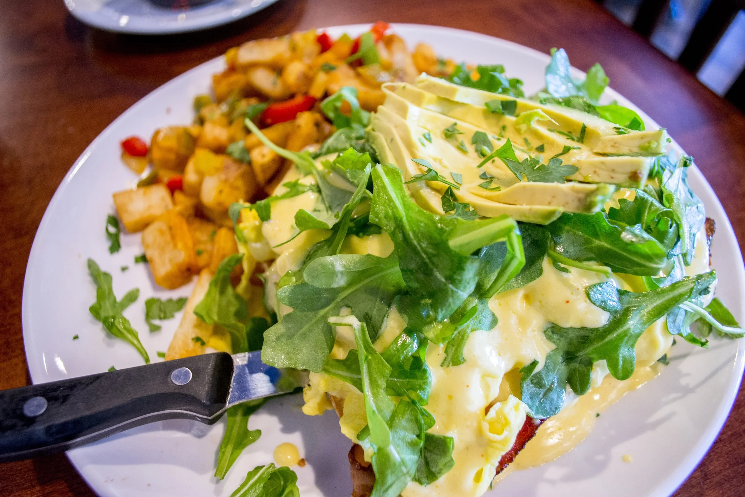   Avocado BLT Benedict ($12.99) features eggs, hickory smoked bacon, grilled tomatoes, hollandaise sauce, lemon dressed baby arugula and sliced avocado over toasted ciabatta bread. It’s served with breakfast potatoes.  
