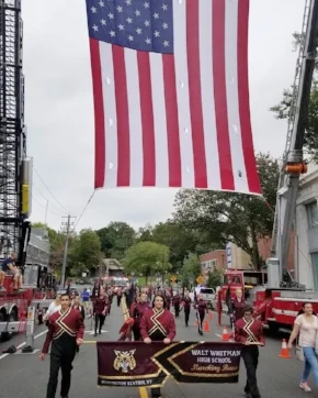 Walt Whitman High School marching band passes under the American flag during Sunday’s Long Island Columbus Day Parade in Huntington. Photo/South Huntington School District