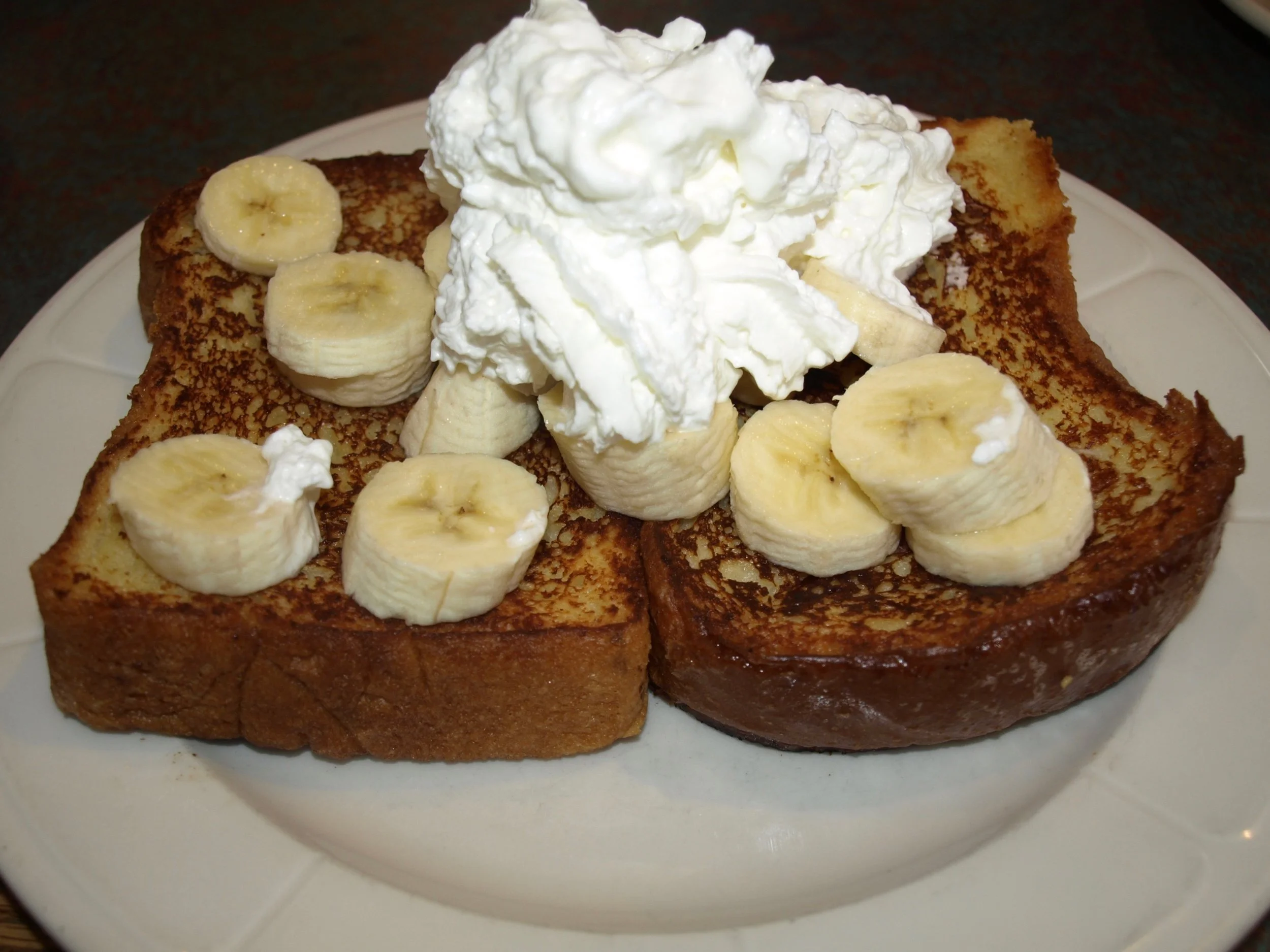  Challah bread French toast is topped with banas and whipped cream. 
