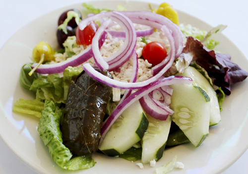  Greek salad of mixed greens, feta cheese, cucumbers, olives, red onions, pepperoncini and grape leaves is topped with house dressing. 