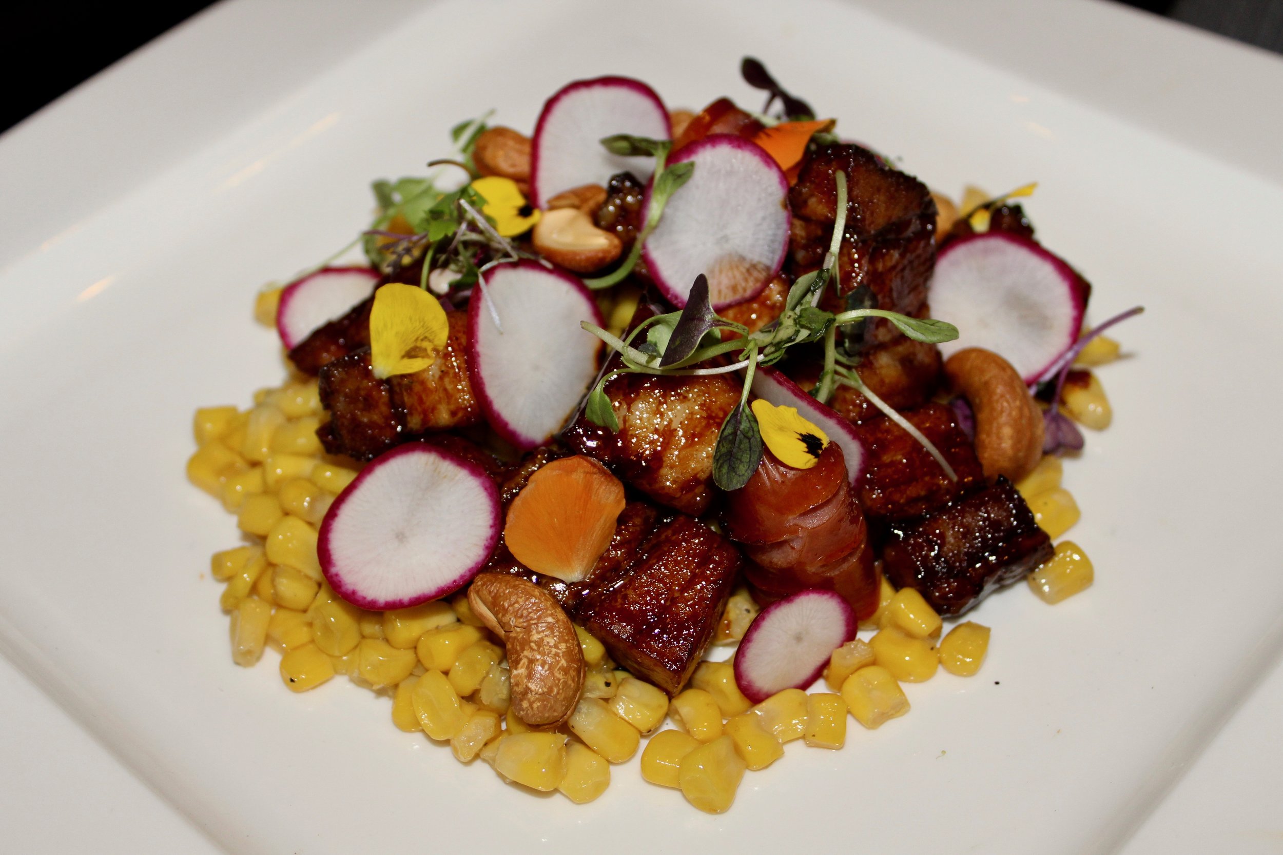 Braised Pork with pork sausage and radishes on a bed of sweet corn.