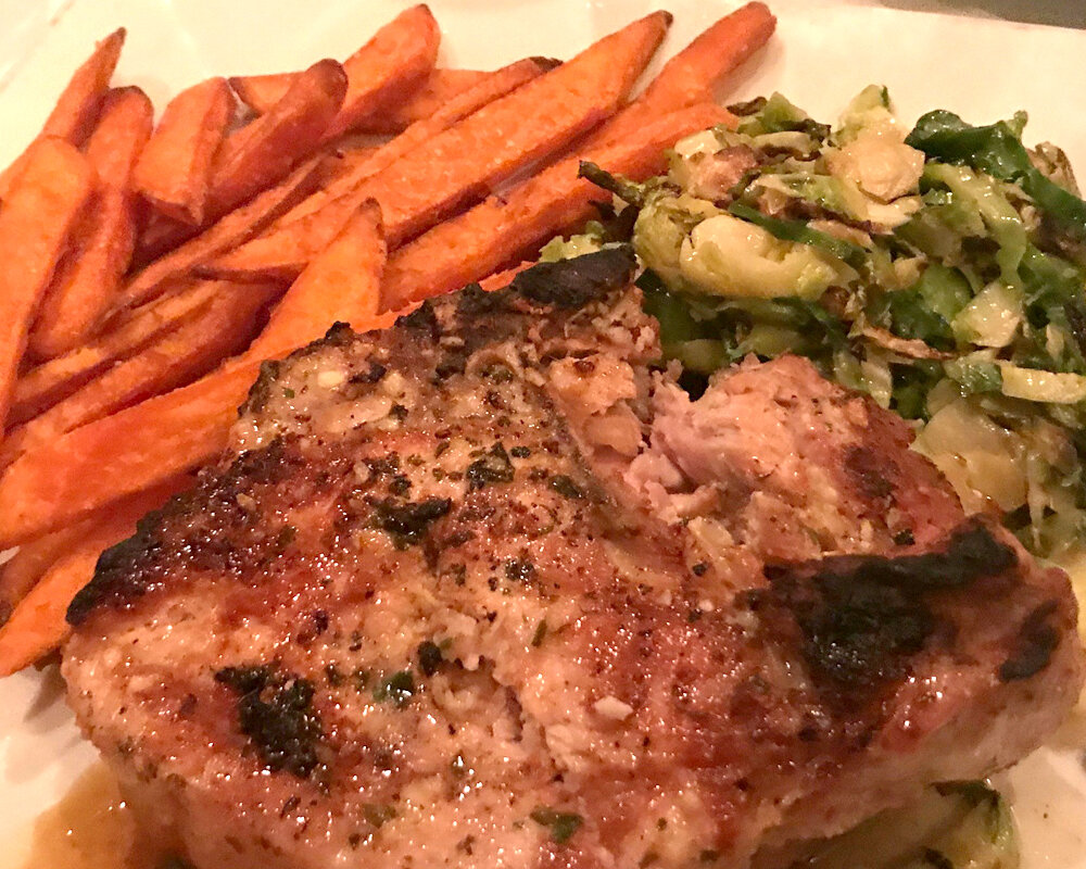  An 18 oz. Grilled Pork Porterhouse with herbed garlic butter, brussel sprouts, and sweet potato fries. 