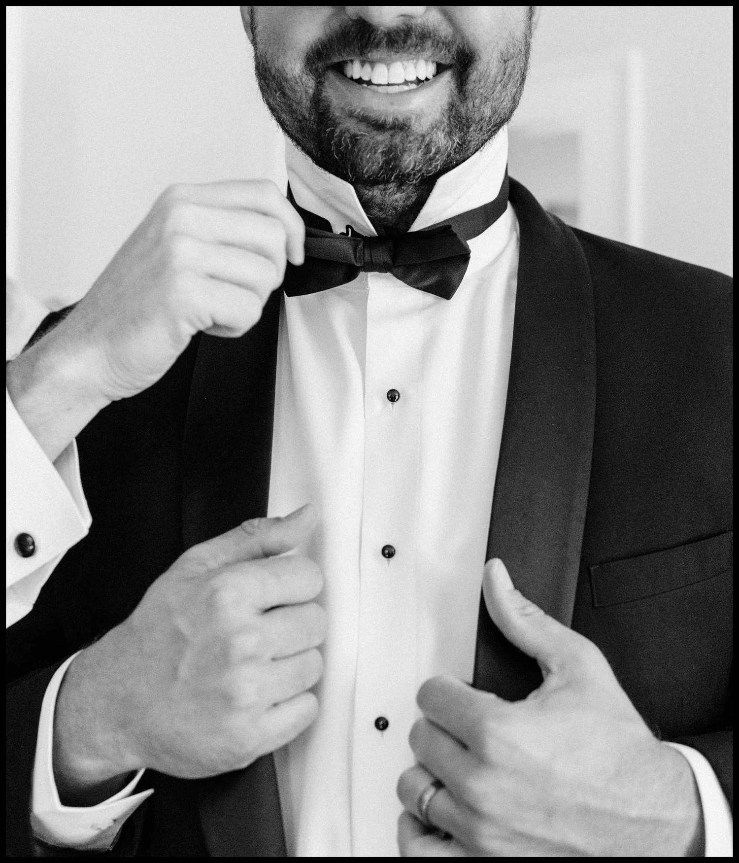 A groom straightening his bow tie, in black and white